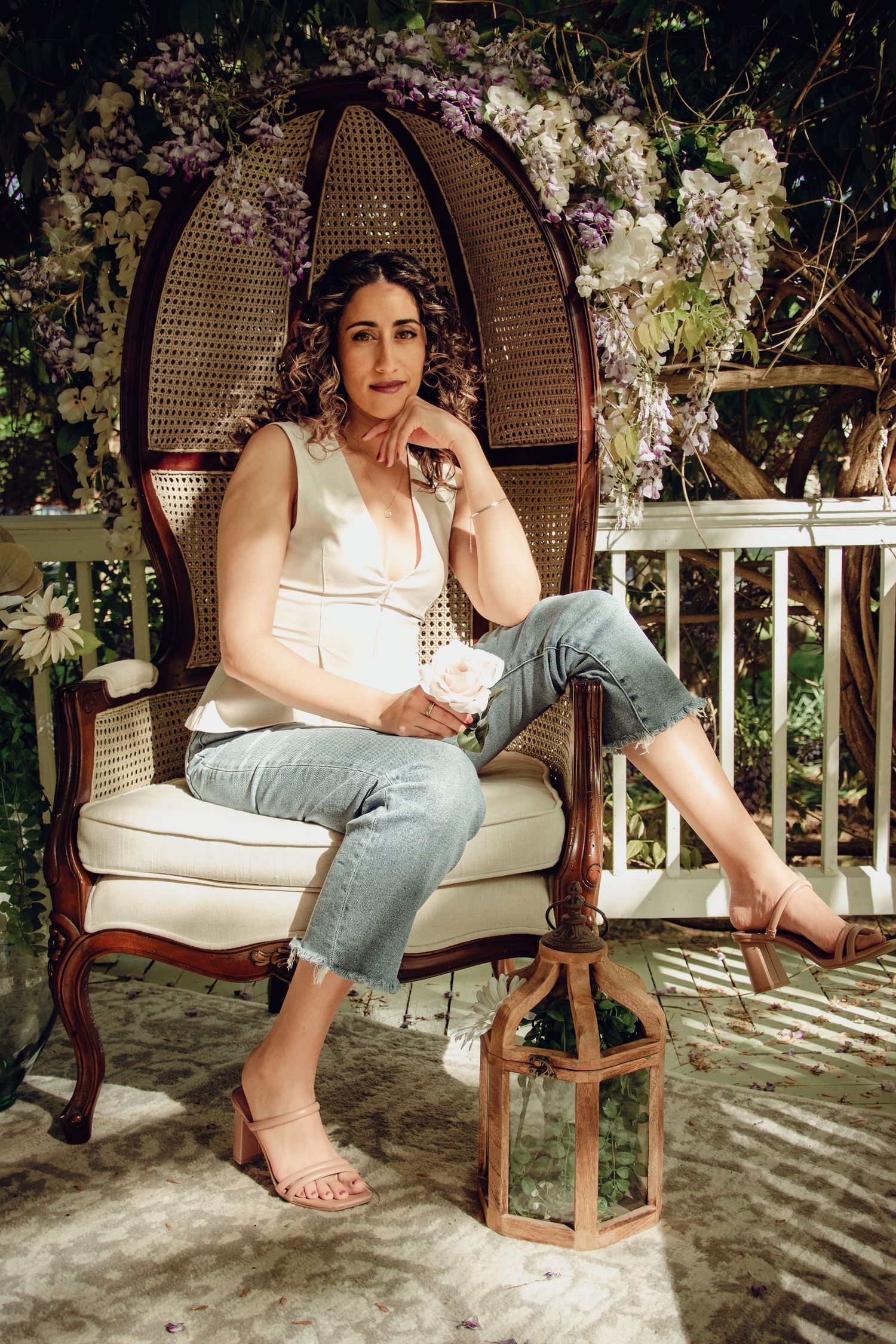 Woman lounges in balloon chair surrounded by floral arrangements on porch. Professional portrait photography.