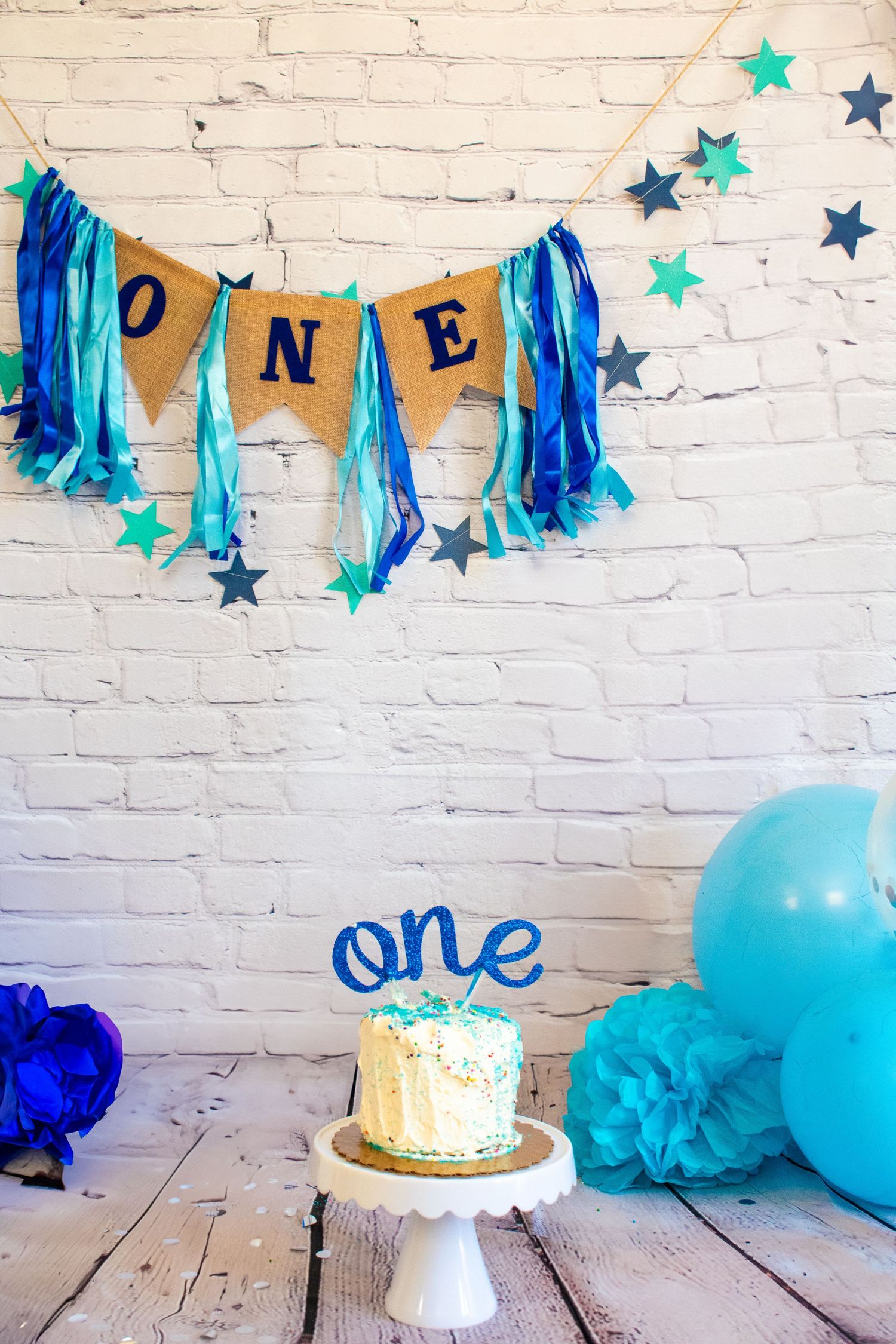 White cake covered with sprinkles with a blue one written in cursive added to the top under blue banner. Professional photography.