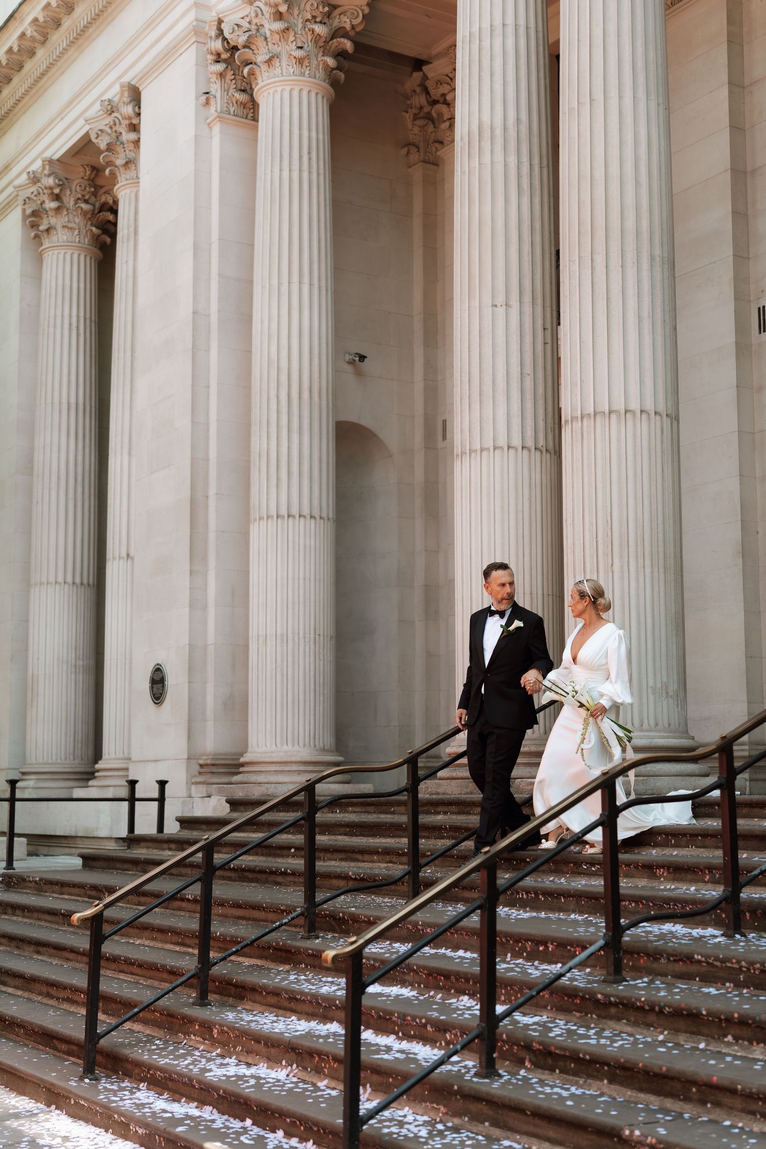 A couple descends grand stone steps with ornate Corinthian columns in the background.