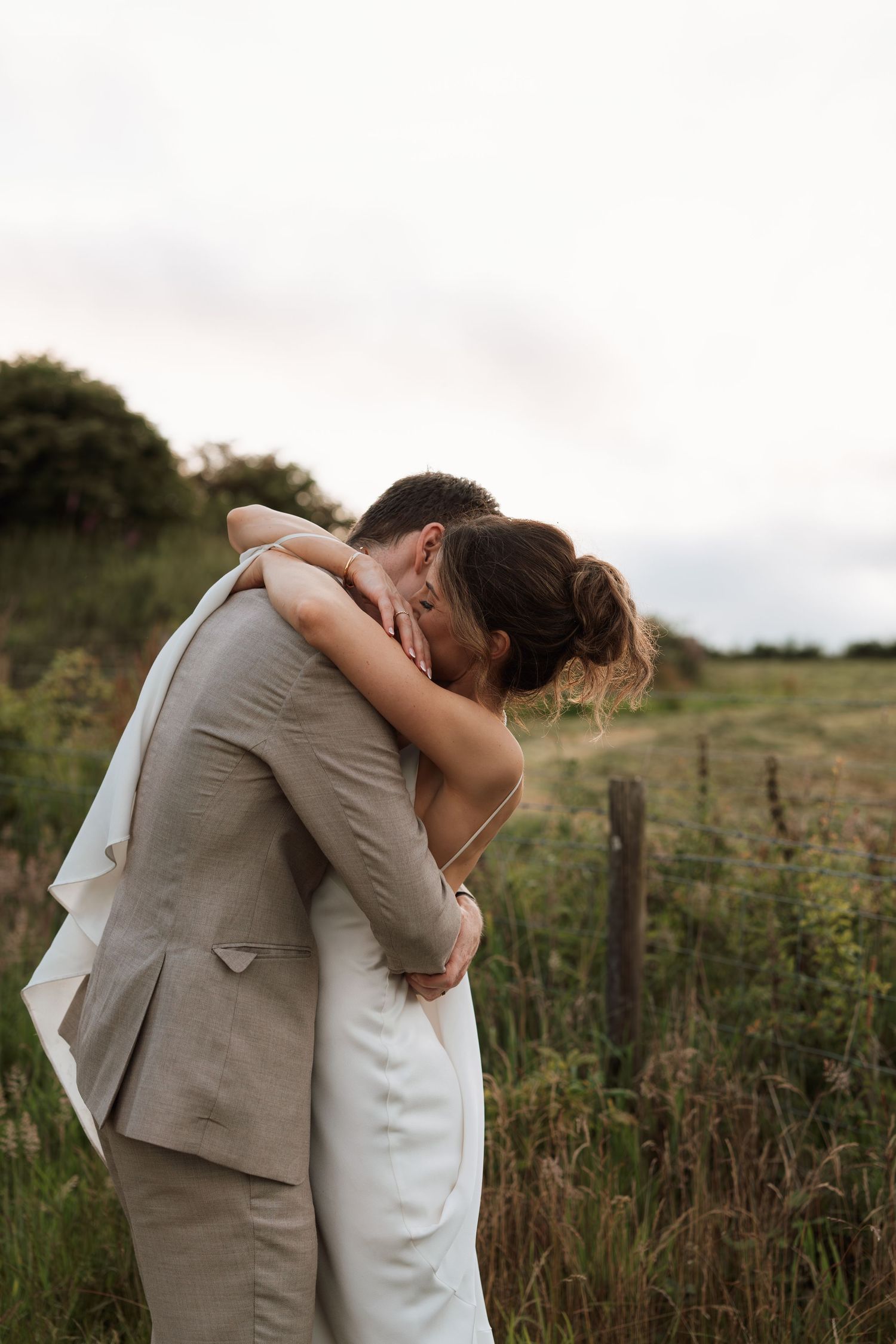 Couple embraces in a romantic moment against a natural outdoor backdrop at sunset.