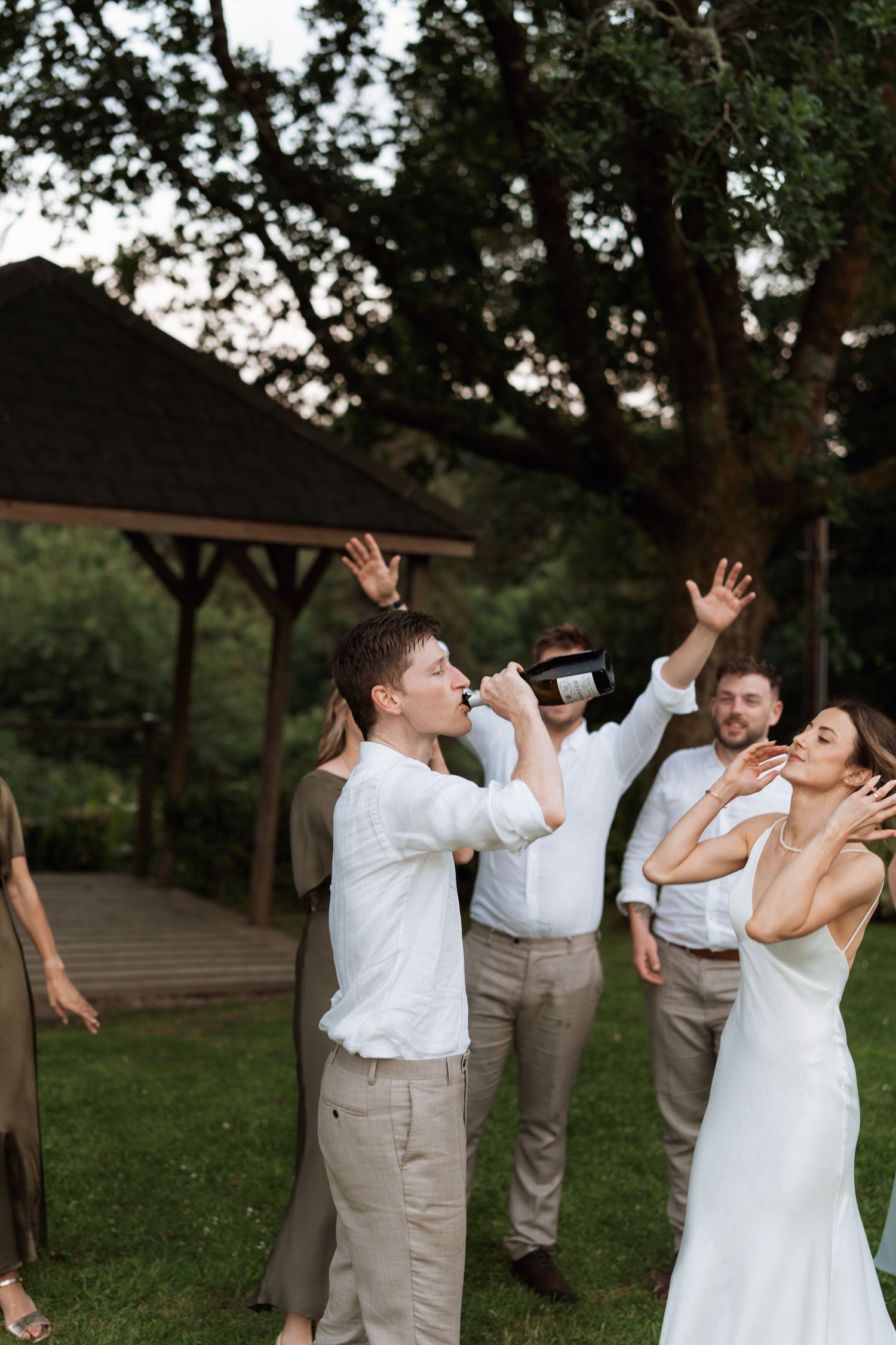Wedding party takes celebratory drinks together on grassy lawn in casual poses.