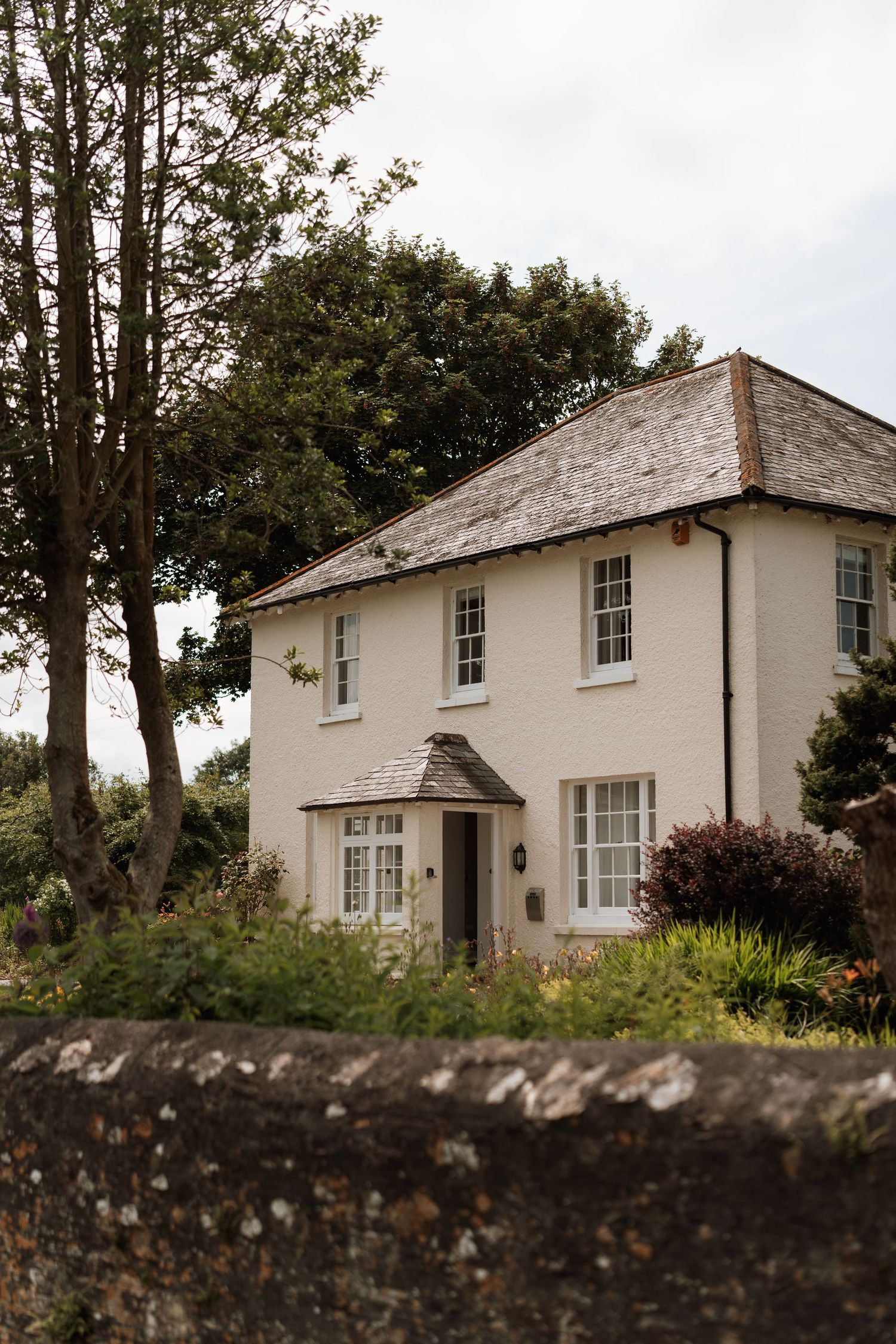 A charming white country house with traditional windows and a sloped roof surrounded by trees.