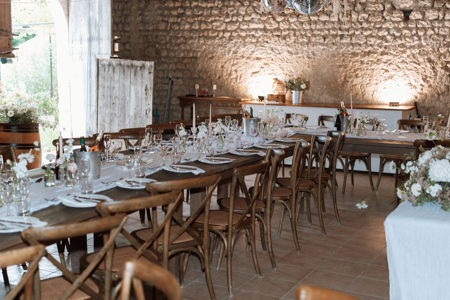 Rustic wedding reception table setup with wooden chairs and elegant place settings in a stone-walled venue.