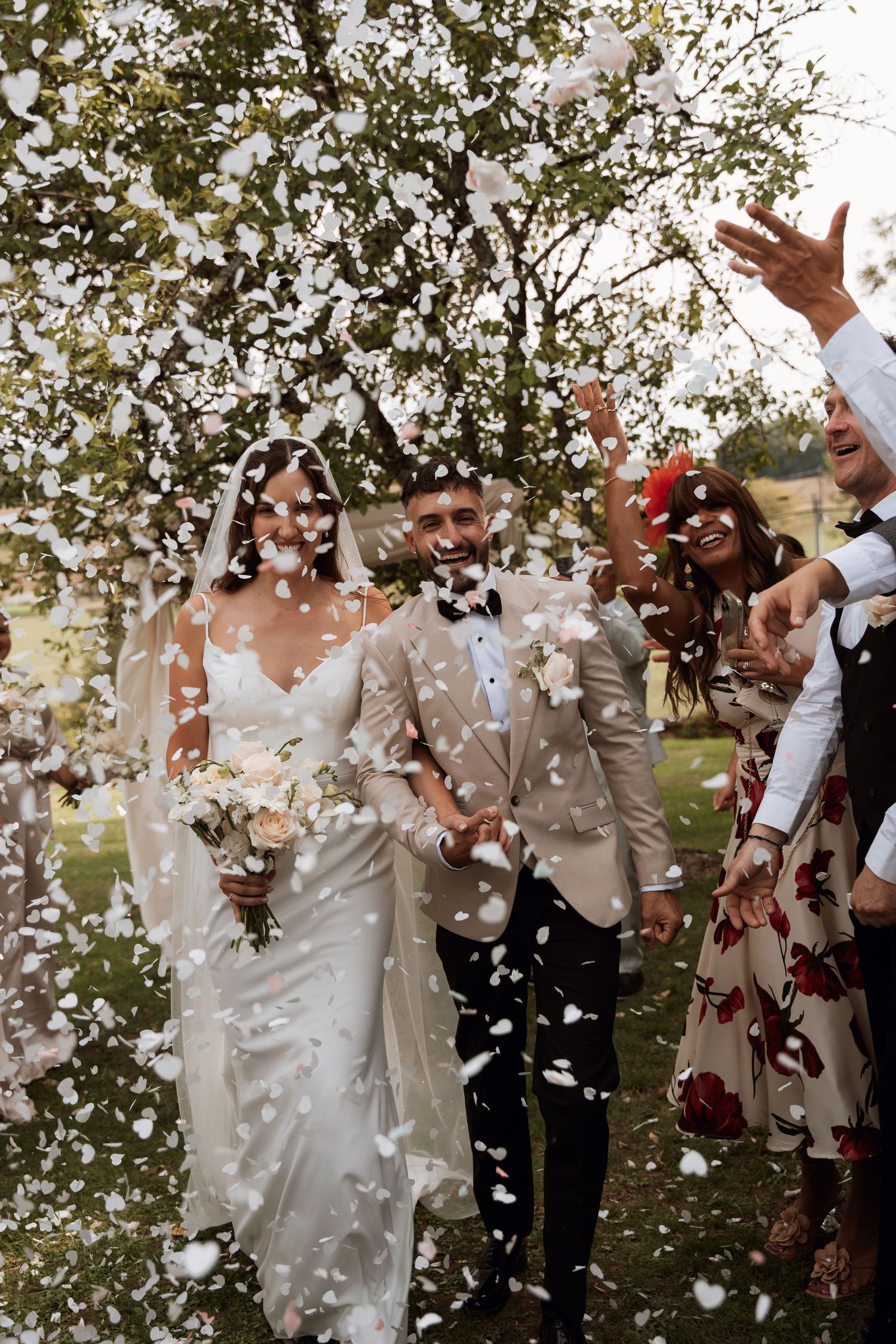 Joyful celebration with white confetti being thrown at an outdoor wedding.