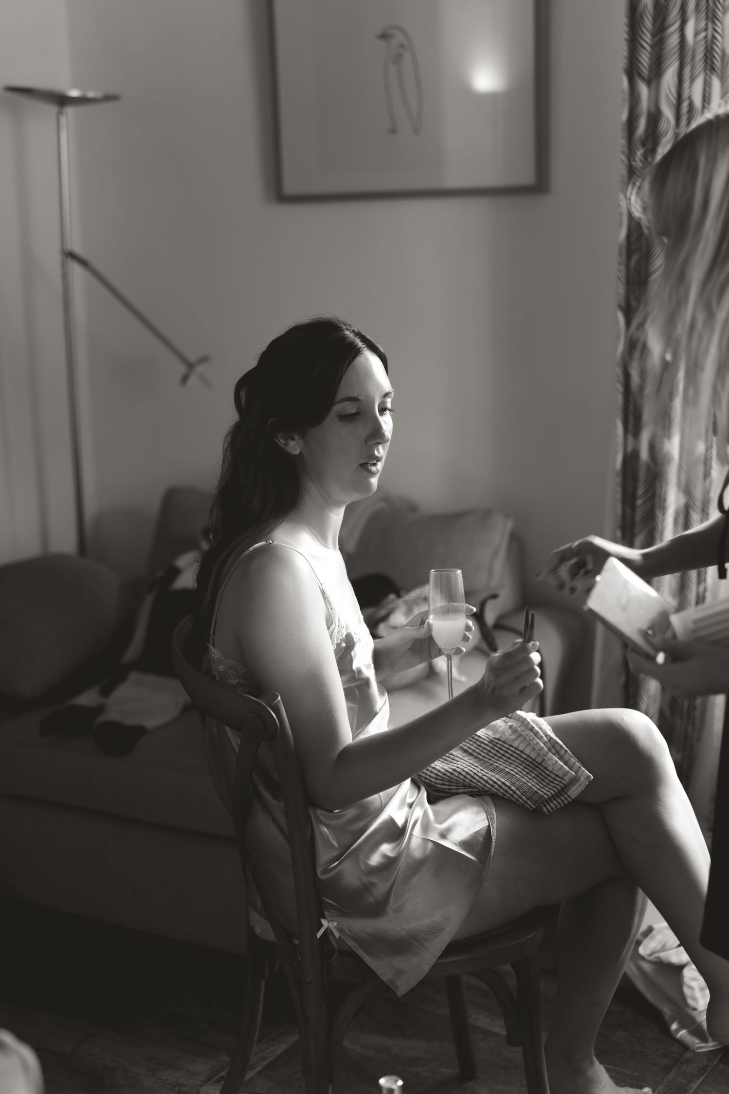 A black and white photograph shows a woman sitting in a chair by a window, reading in natural light.