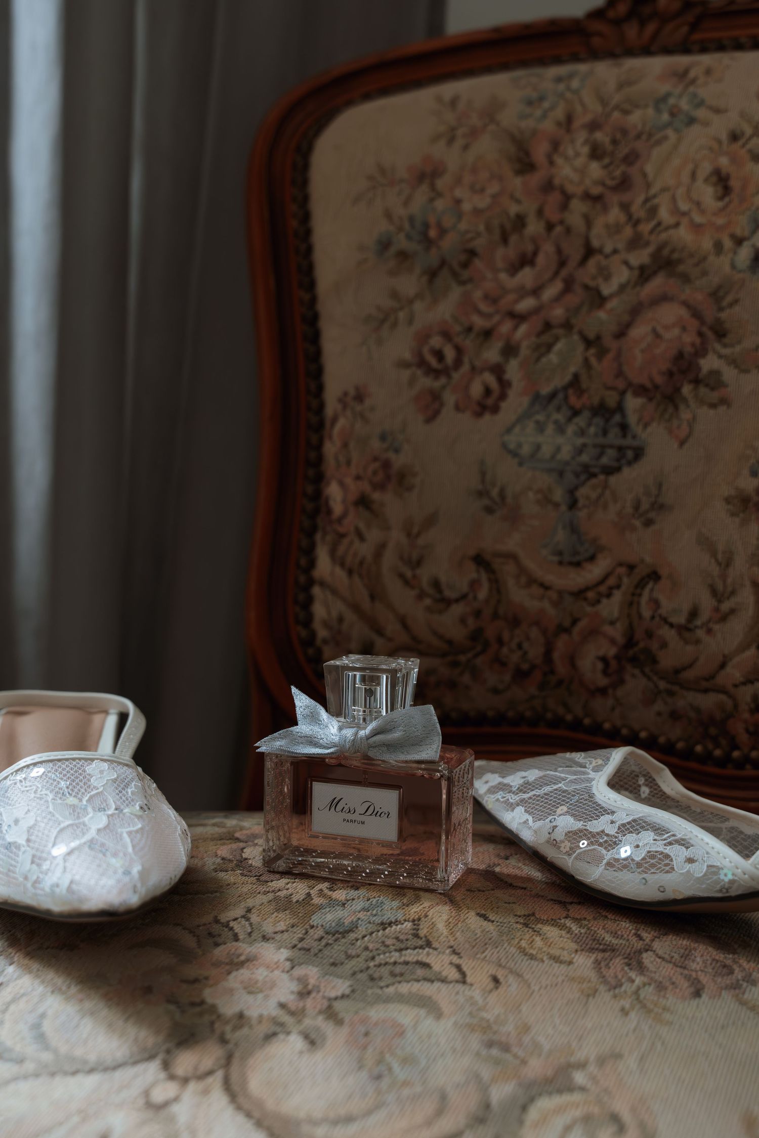 A series of vintage lace and fabric items arranged on an antique table with ornate chairs in the background.