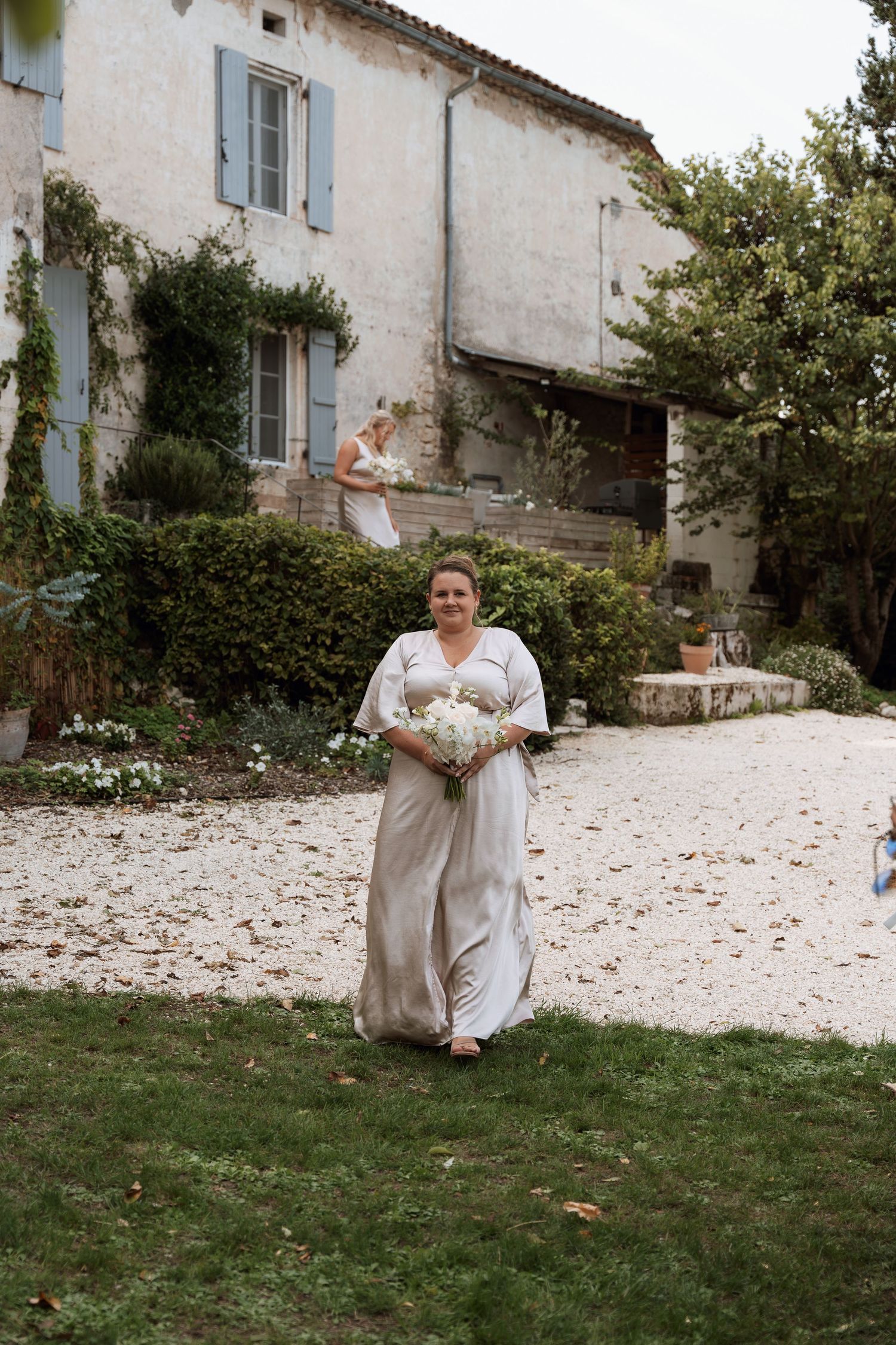 A person in formal attire sits on grass outside a stone building.
