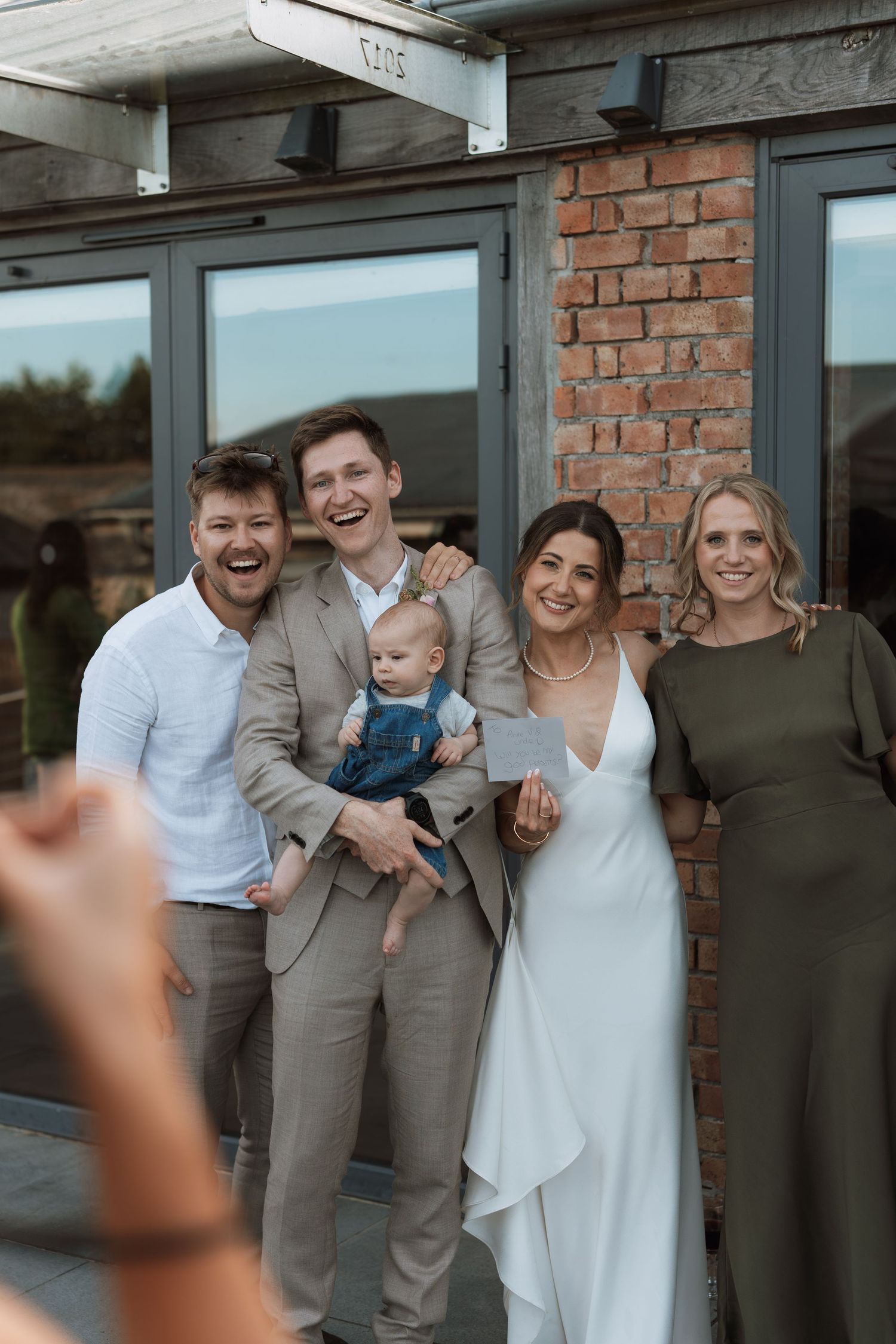 Wedding party poses together for a joyful group photo outside a brick building.