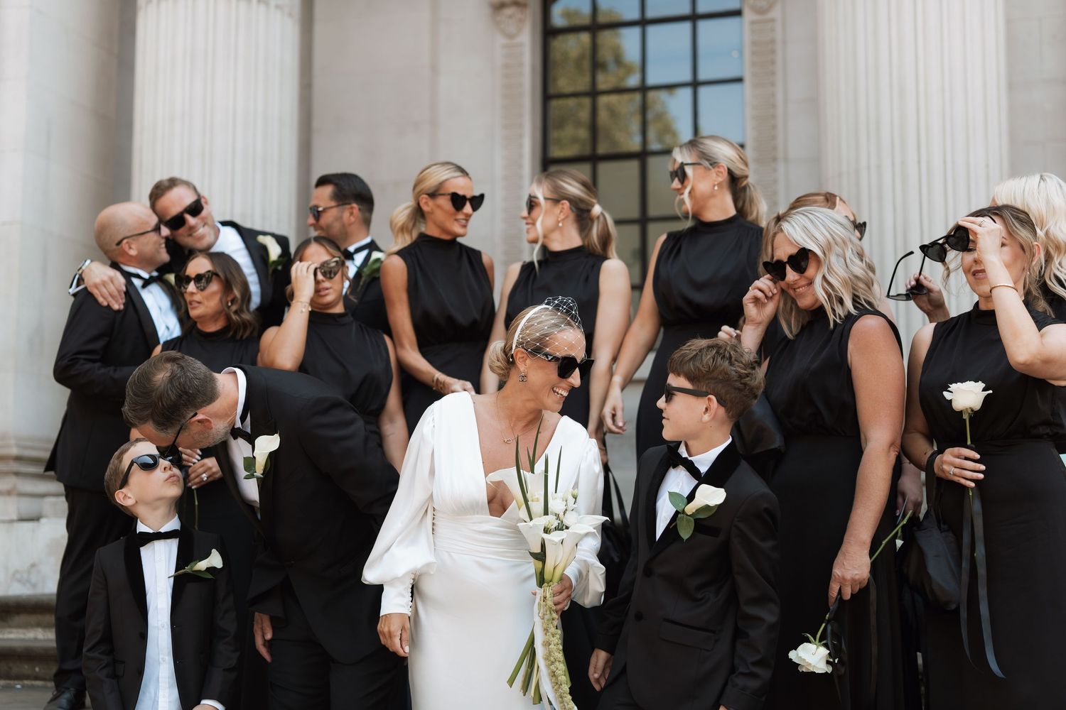 Wedding party in black and white attire gathered in front of classical white columns.