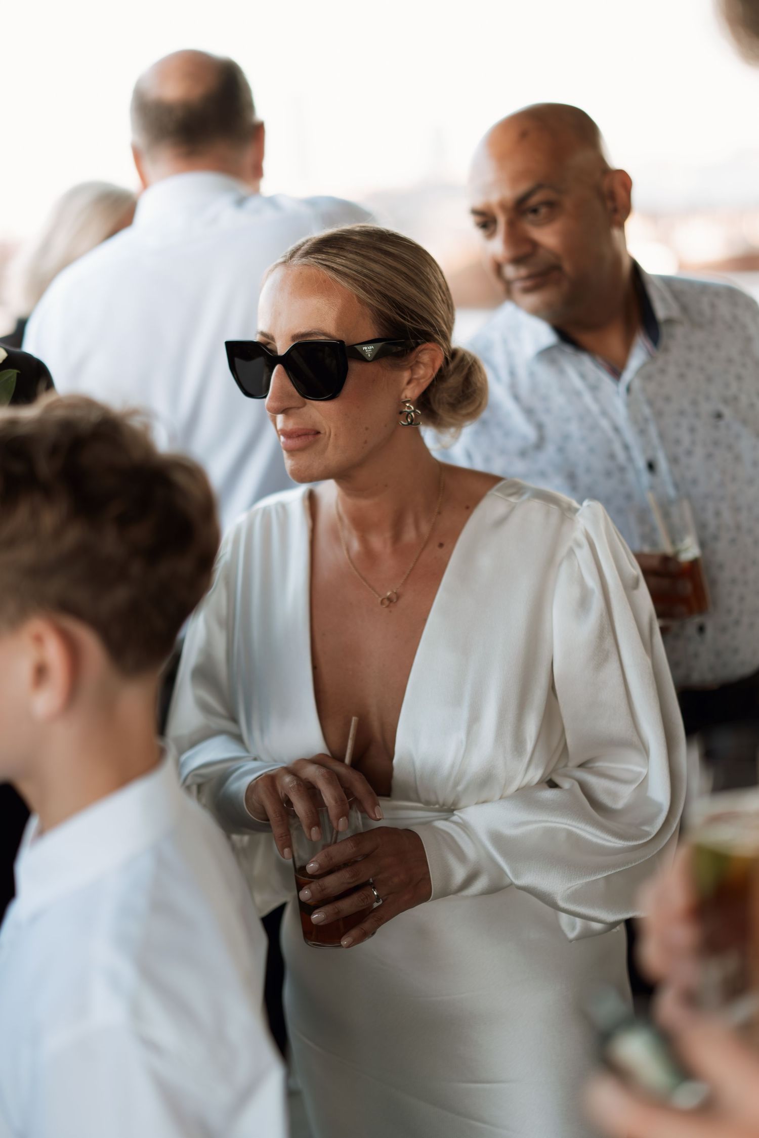 Wedding reception guests mingling in elegant white attire and sunglasses.