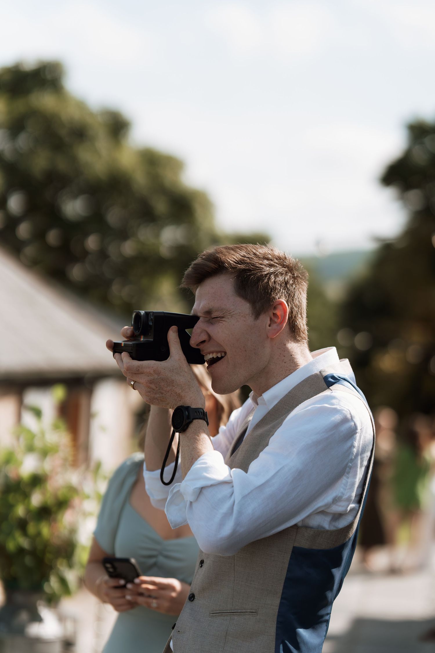 Photographer in a light colored vest captures candid moments at an outdoor event.
