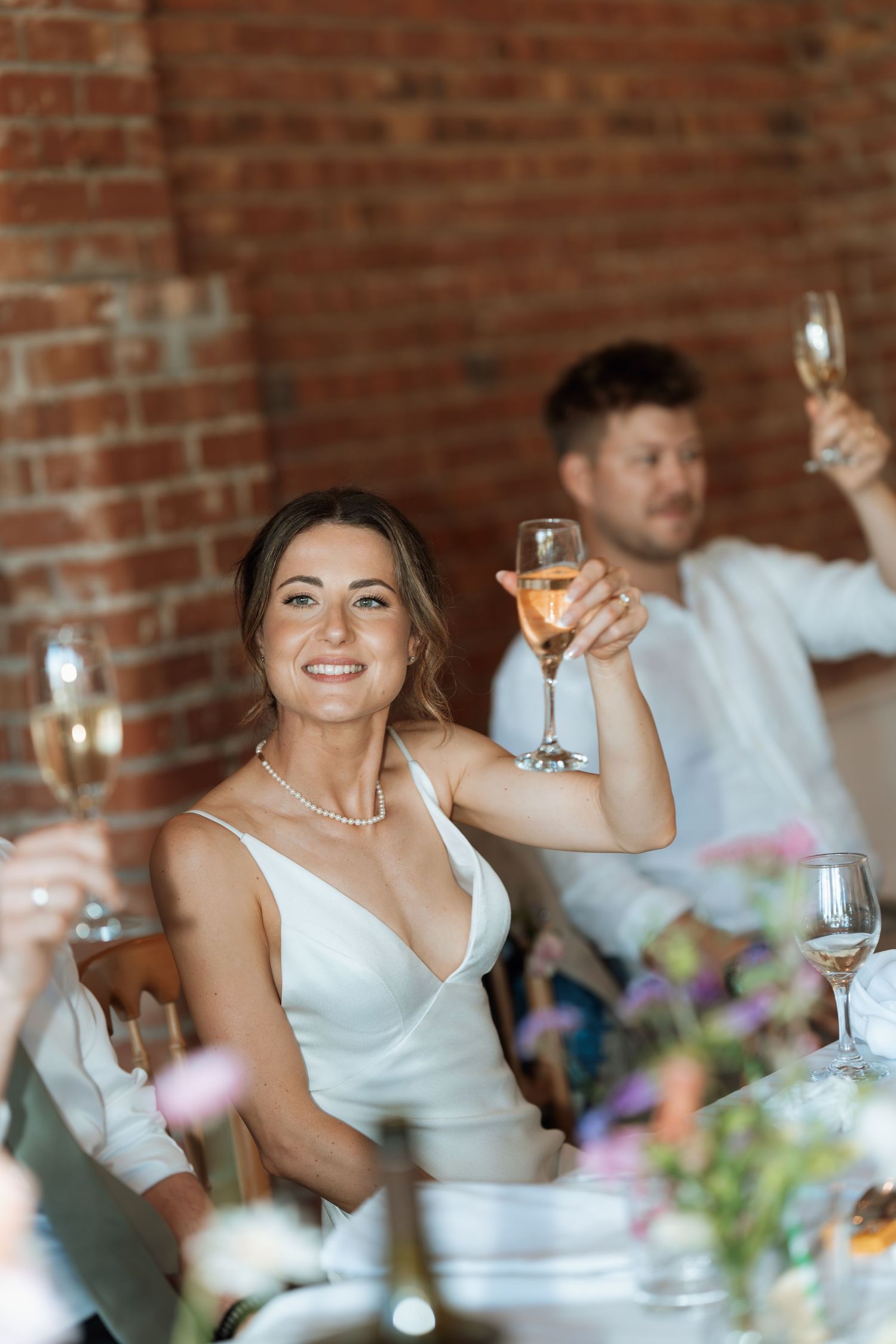 Wedding reception table setting with champagne glasses and pink floral centerpieces against brick walls.