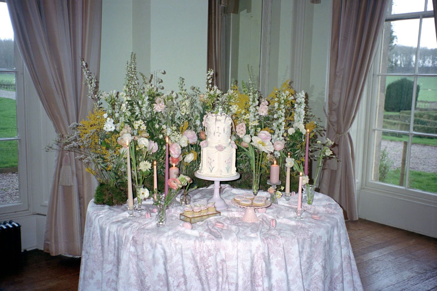 Elegant wedding reception tables decorated with white linens, floral centerpieces, and crystal candelabras in a bright sunlit room.