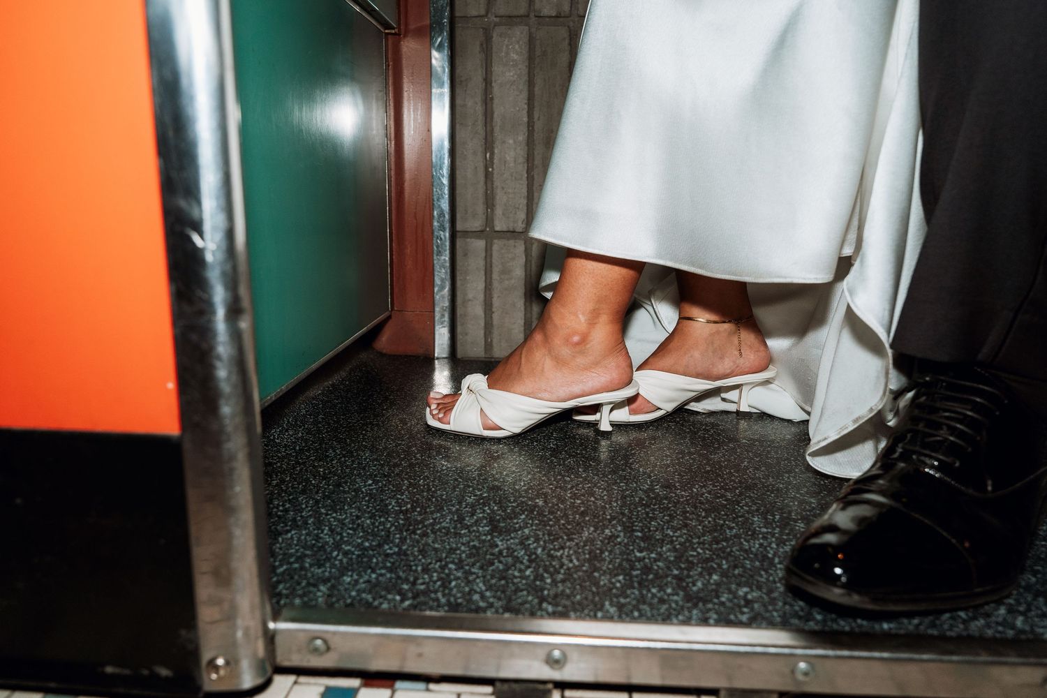 Close-up of formal footwear and dress hem in doorway with black floor.