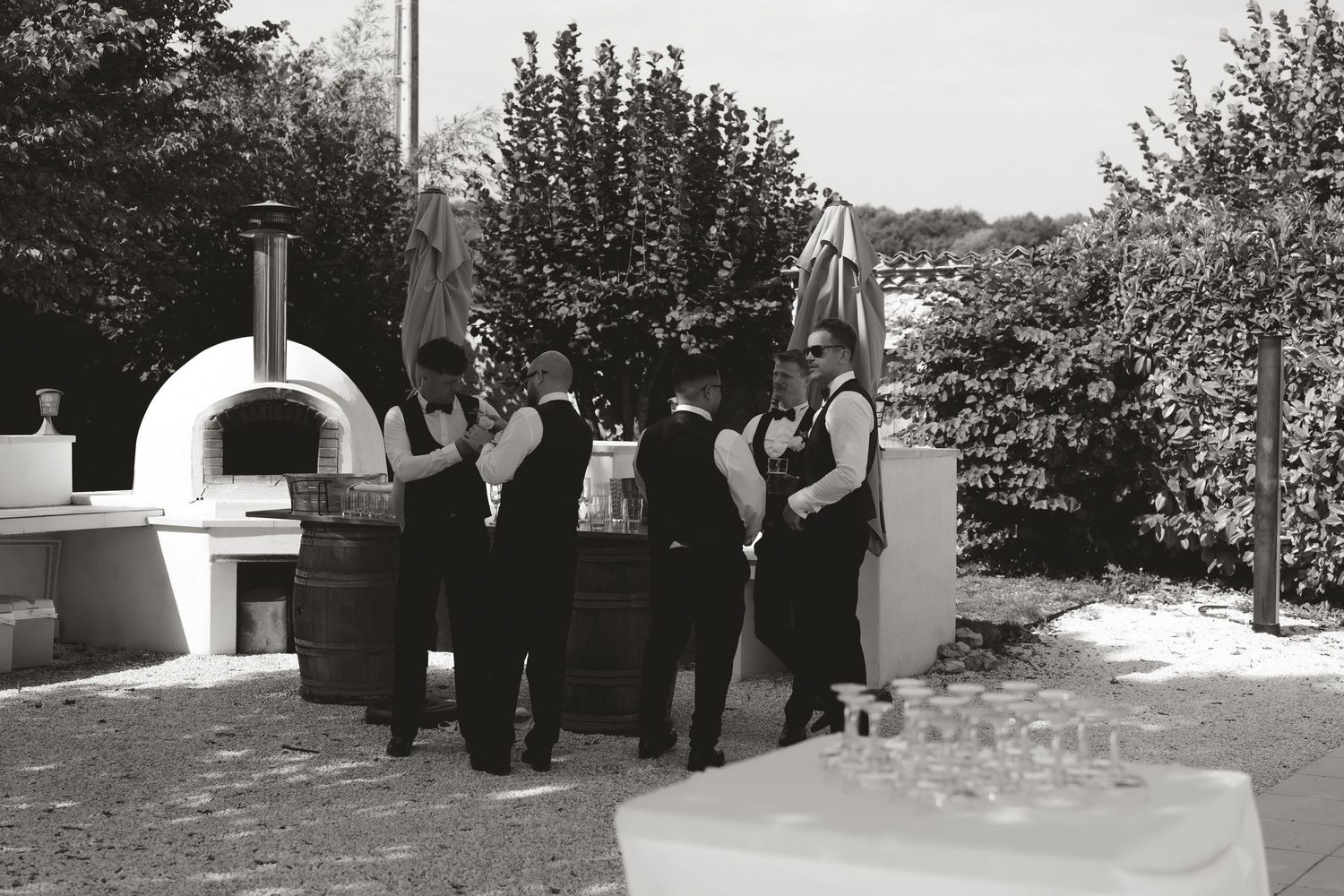 A black and white panoramic view of people gathered outside near trees and a building.