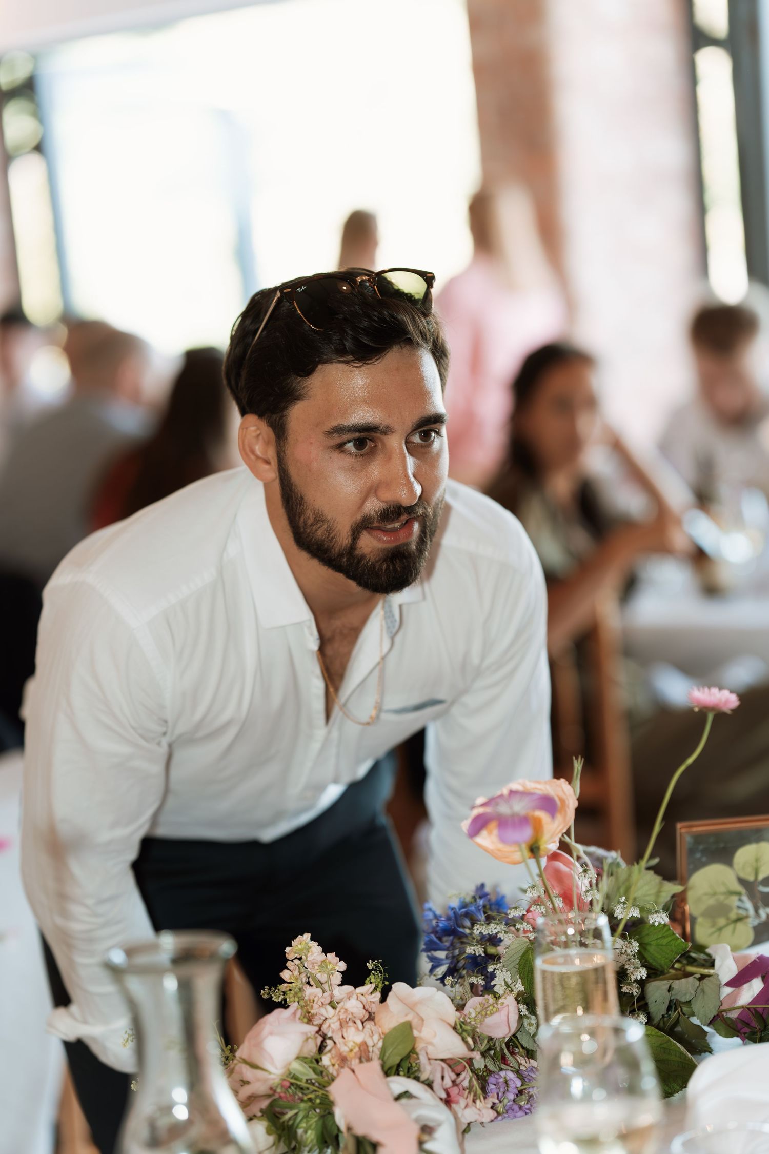 Wedding guest in white shirt leaning over floral table arrangements at reception.