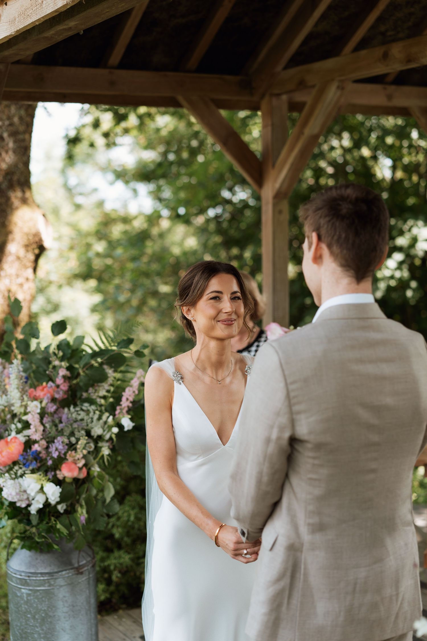 Outdoor wedding ceremony under a rustic wooden pavilion with floral decorations.