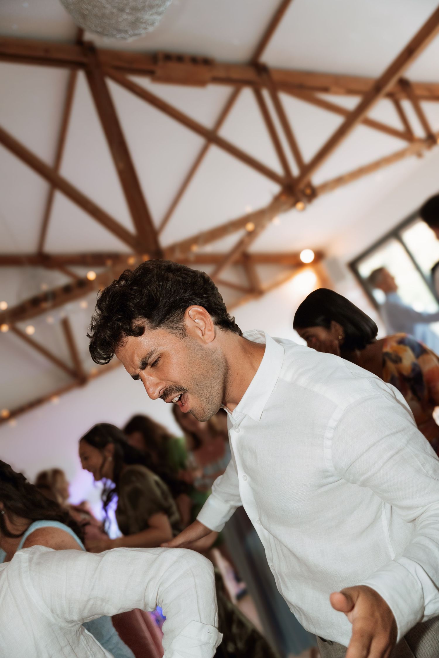 Dancing guests enjoying themselves under wooden beams at an indoor celebration.