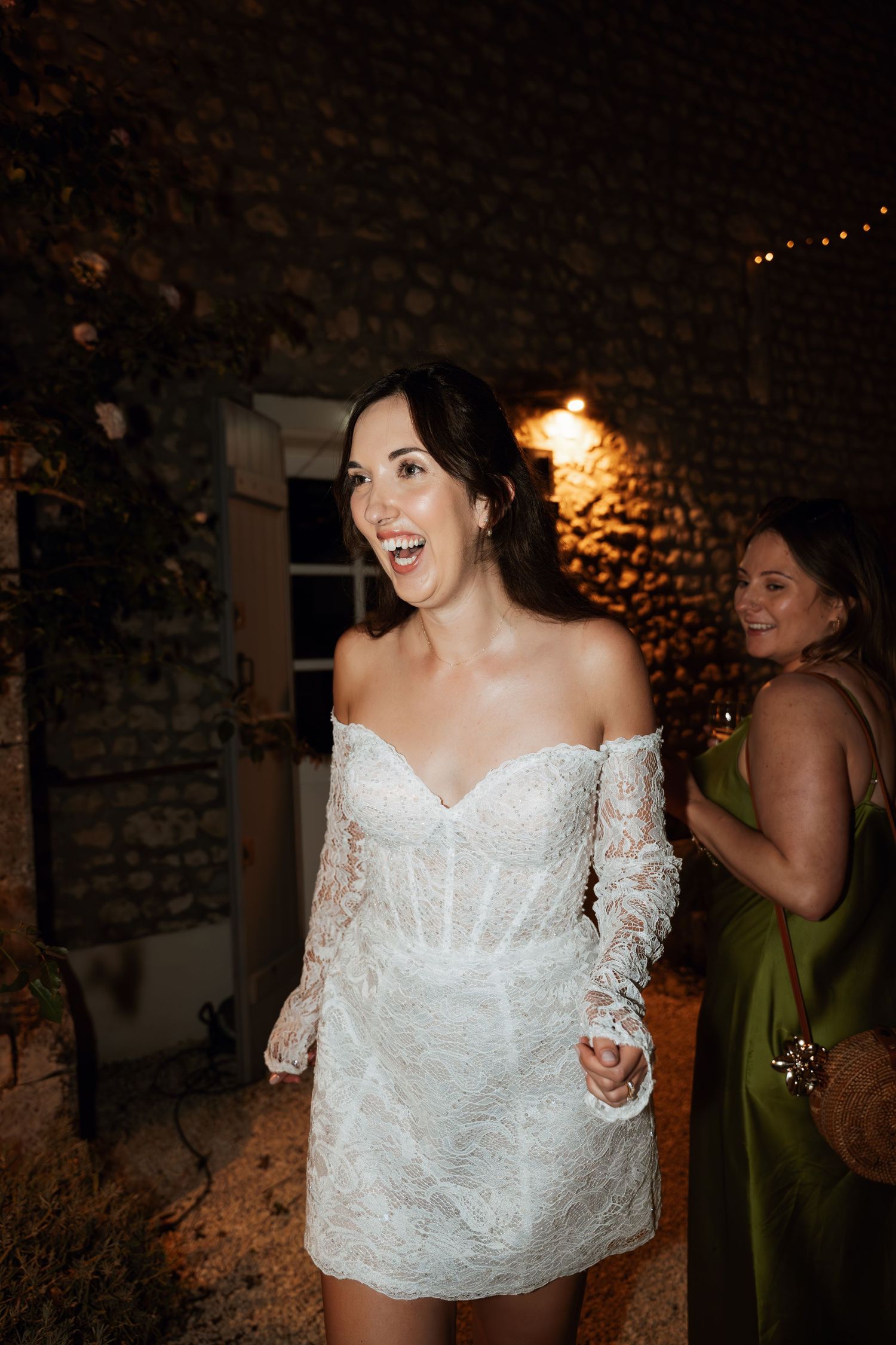 A bride in a beautiful lace wedding dress laughs joyfully during reception celebrations.