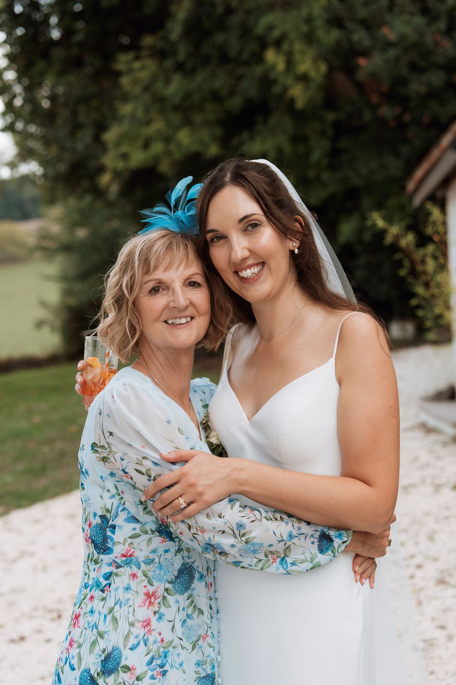 Two women in white and floral dresses share joyful embraces during a wedding celebration.