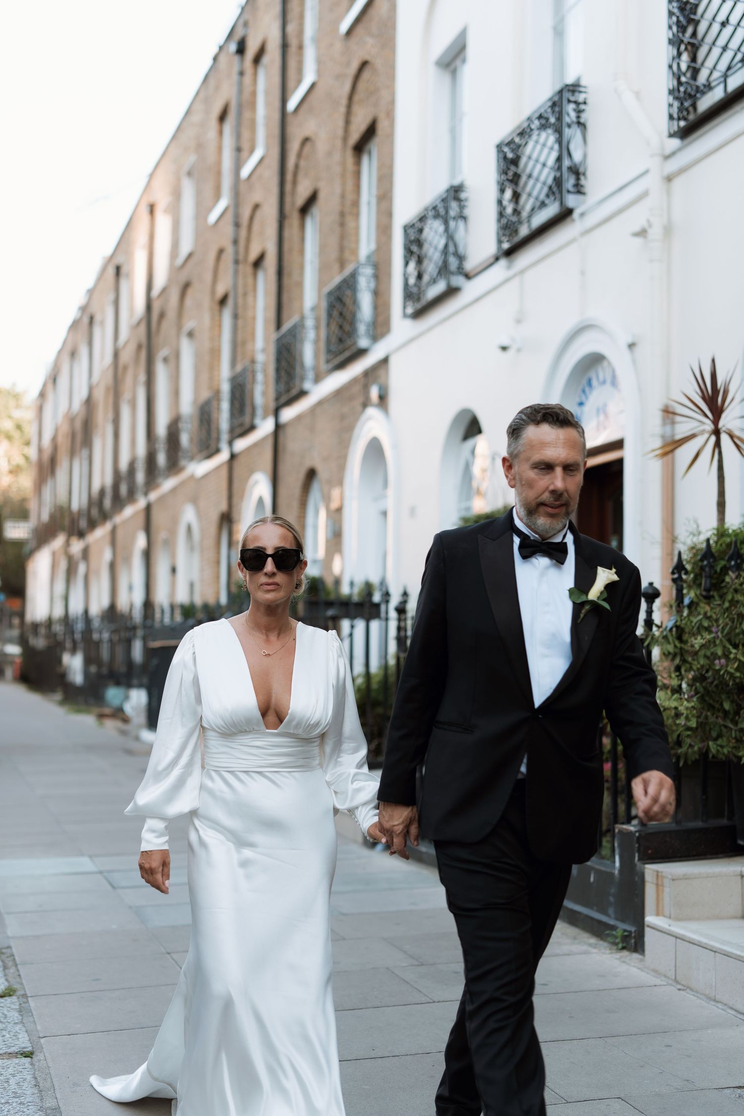 Wedding couple walking together on a sidewalk with classic brick buildings in the background.
