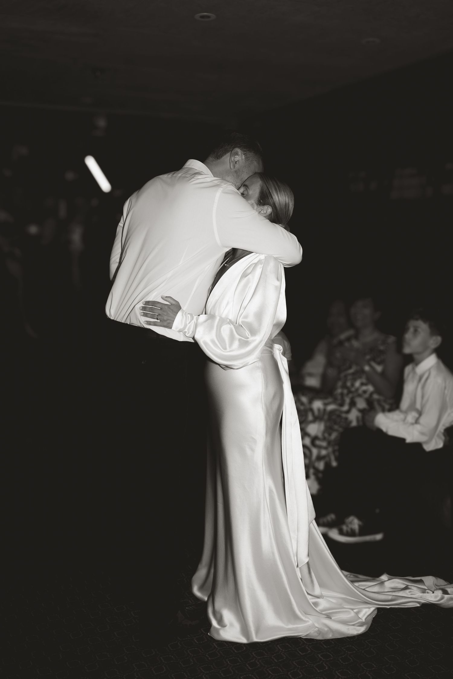 Black and white photo of a bride kneeling in a flowing white wedding dress.