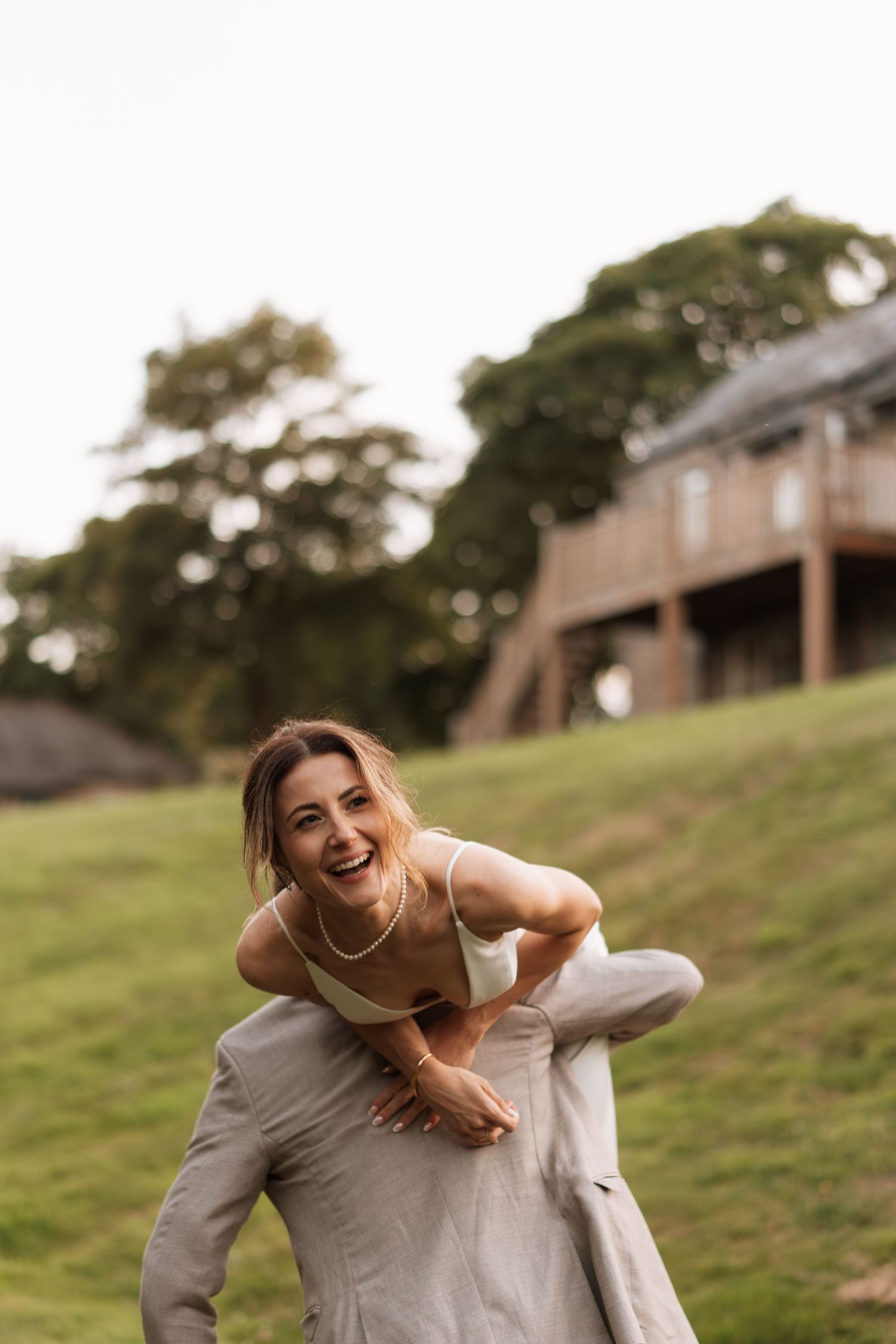 A playful piggyback ride moment captured during outdoor wedding photos on a grassy hillside.