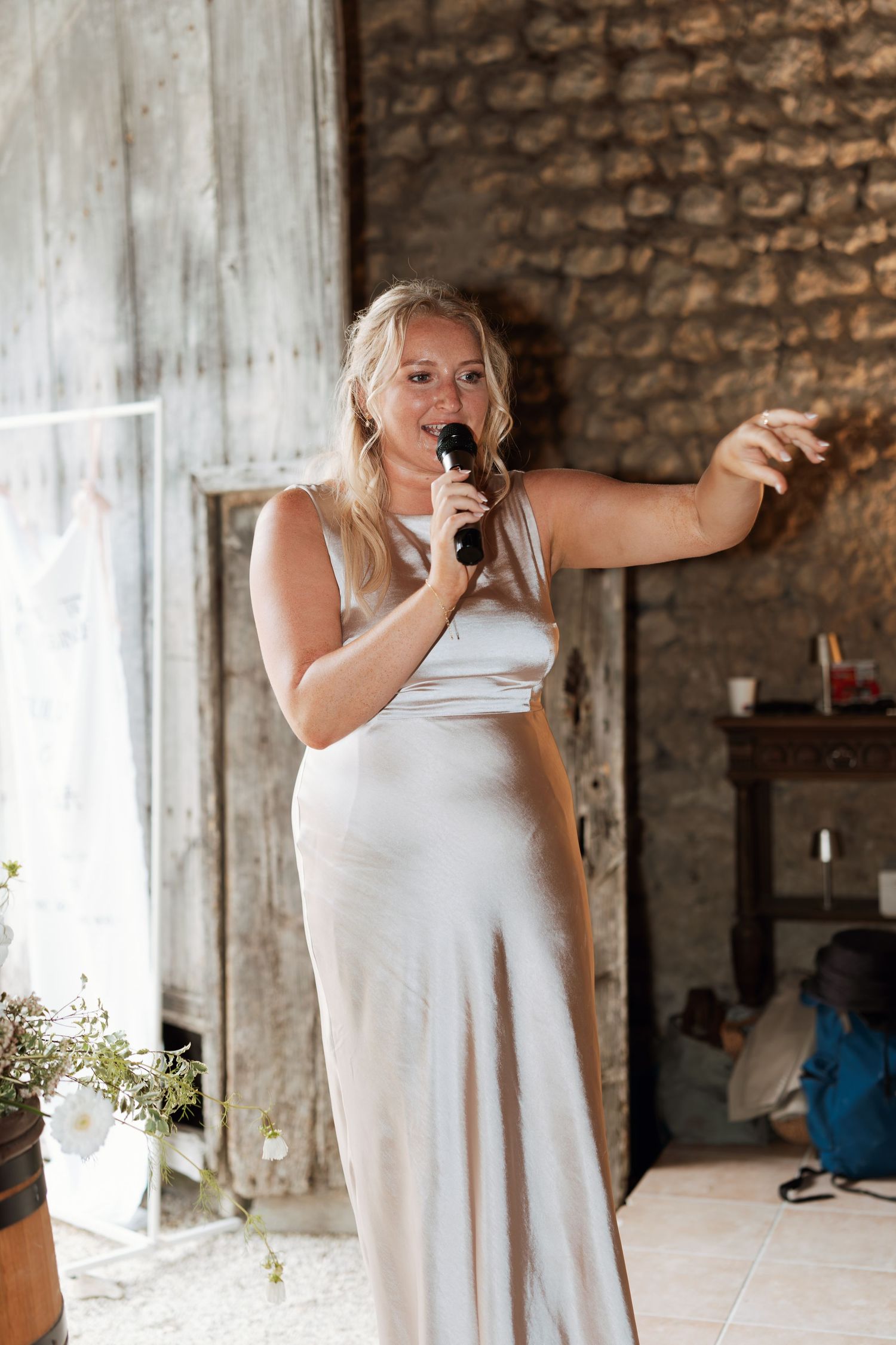A person in white dances joyfully in an industrial-style venue with stone walls.