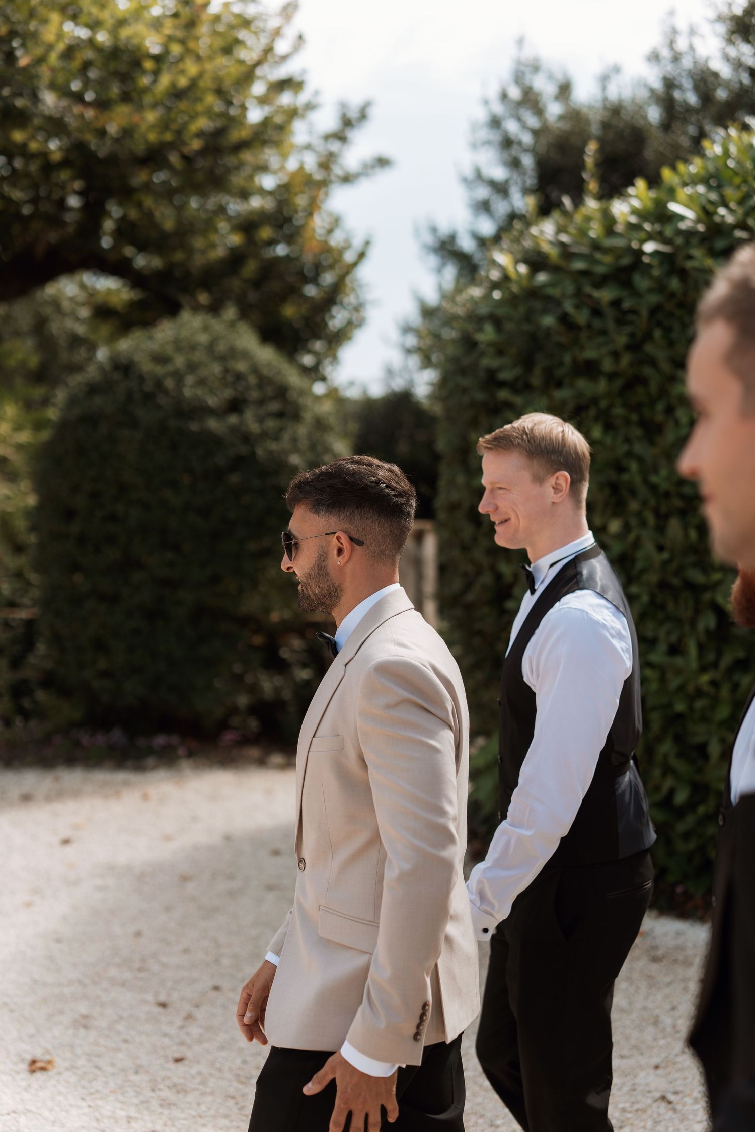 Groomsmen in formal attire share a lighthearted moment outdoors during a wedding celebration.