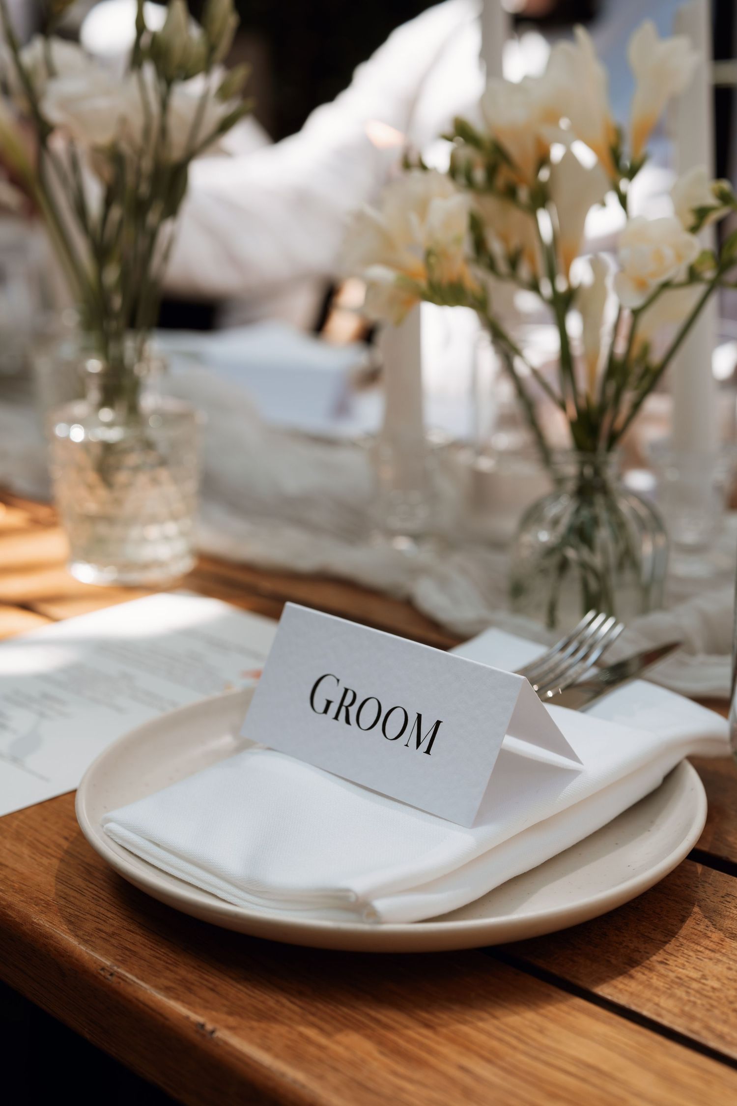 Elegant place setting with groom card and white flowers on wooden table.
