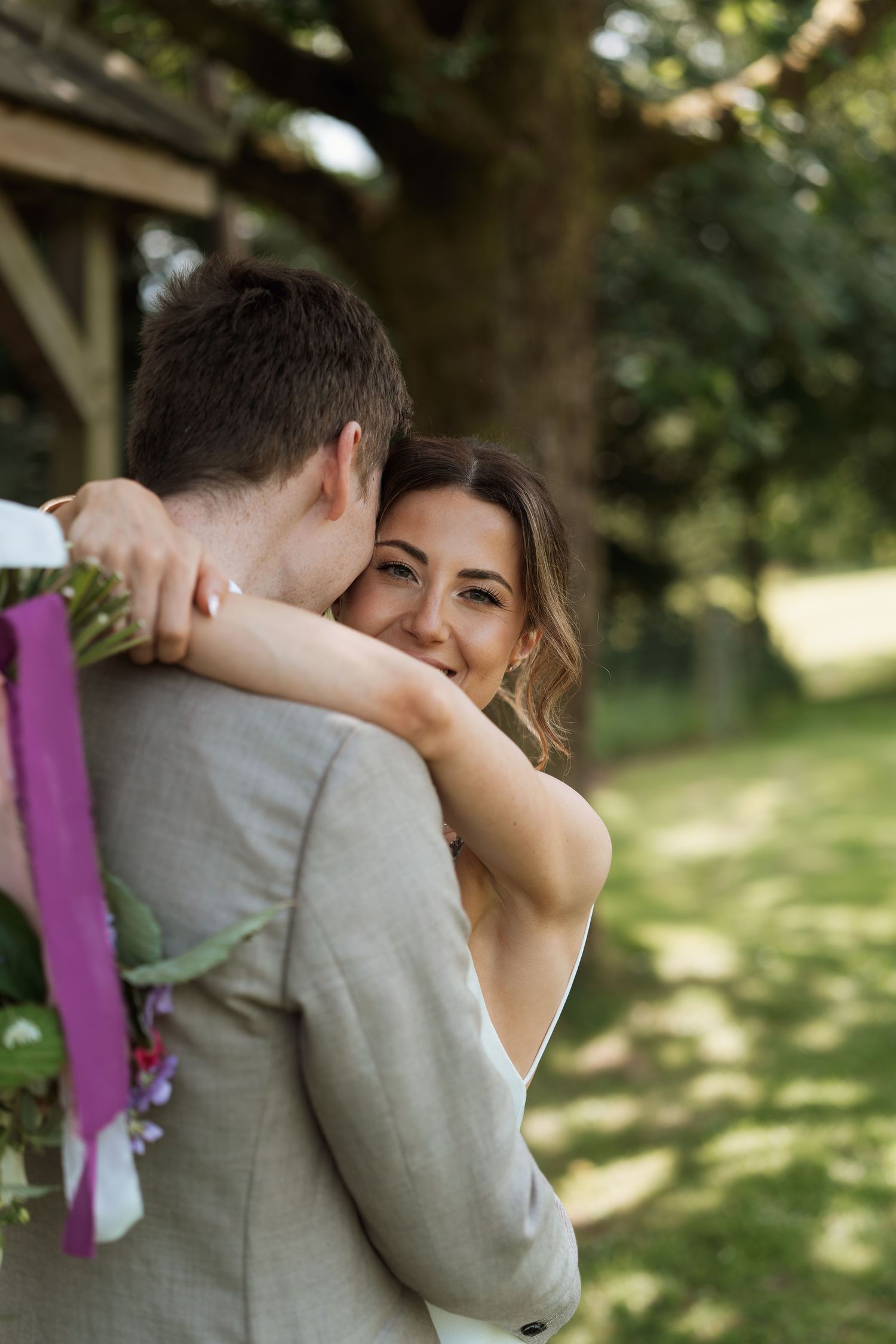 A tender embrace between newlyweds during an outdoor wedding photoshoot in a garden setting.