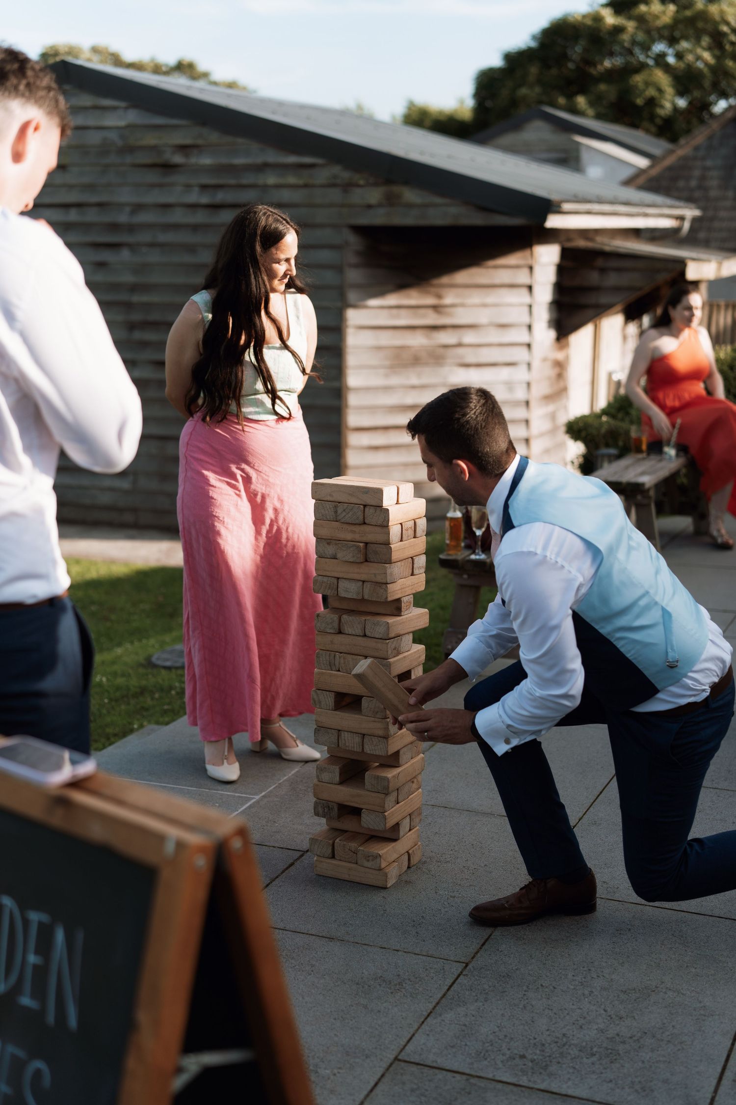 Wedding guests play giant Jenga outdoors during reception festivities.