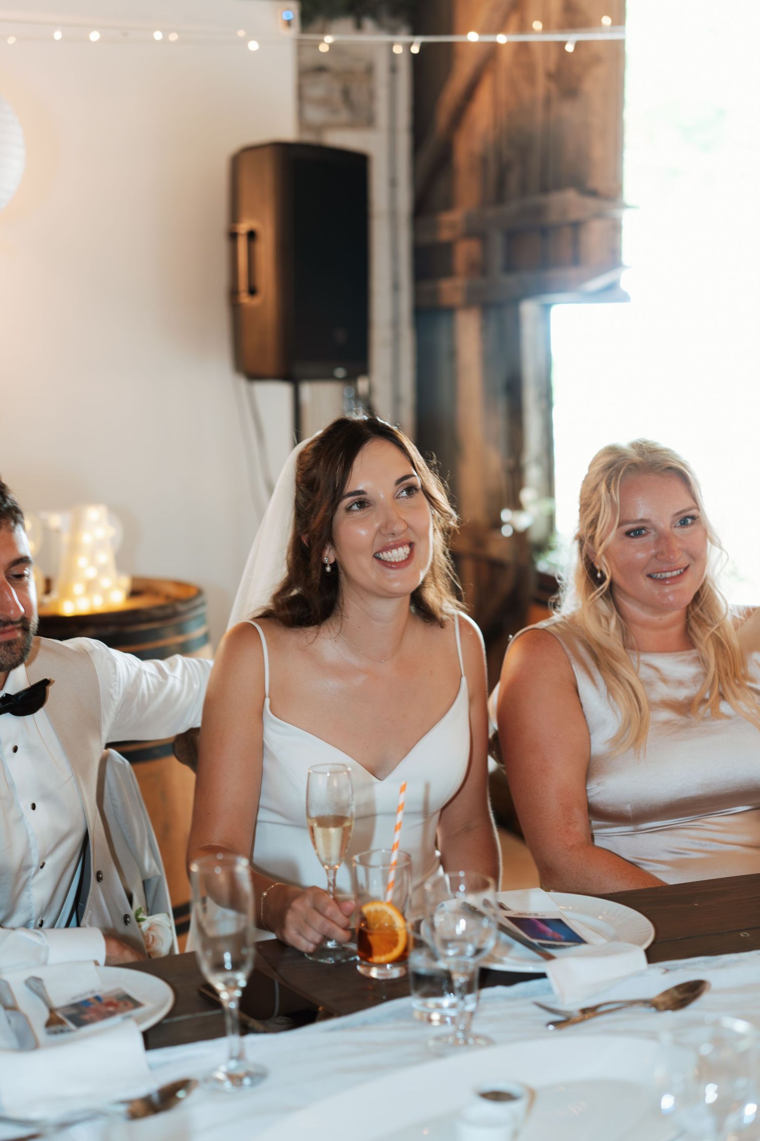 Wedding guests seated at a reception dinner table with string lights visible in the background.
