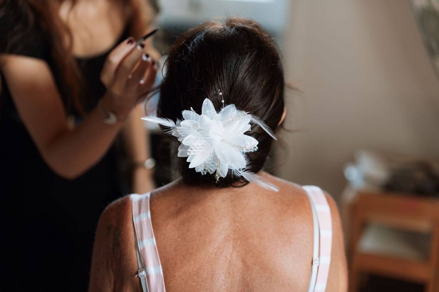 A bride in a white dress and floral hair accessory is seen from behind during wedding preparations.