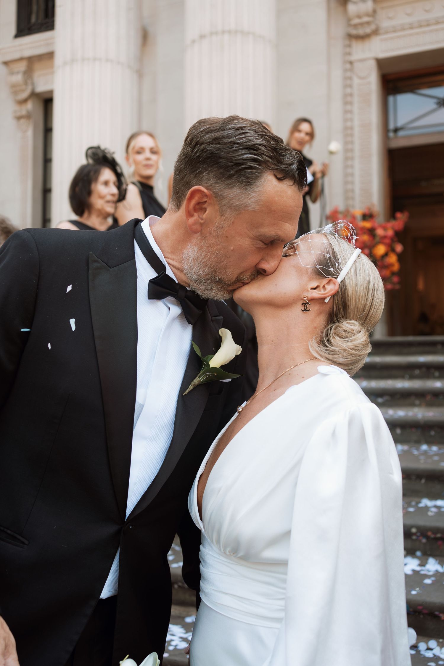 Romantic wedding couple shares a kiss outside a classic architectural building.