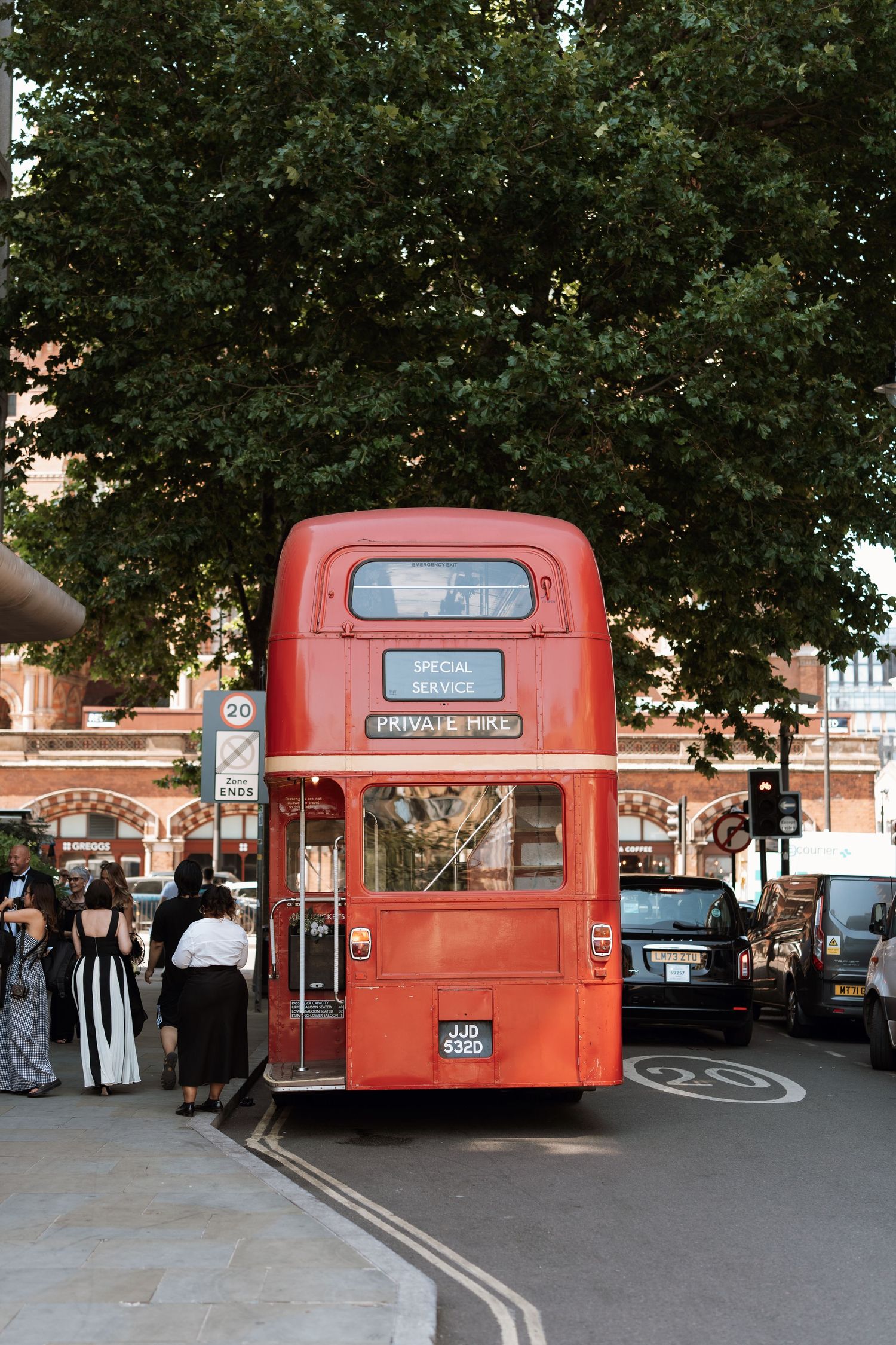 Classic red double-decker bus parked on a London street with trees and buildings in the background.