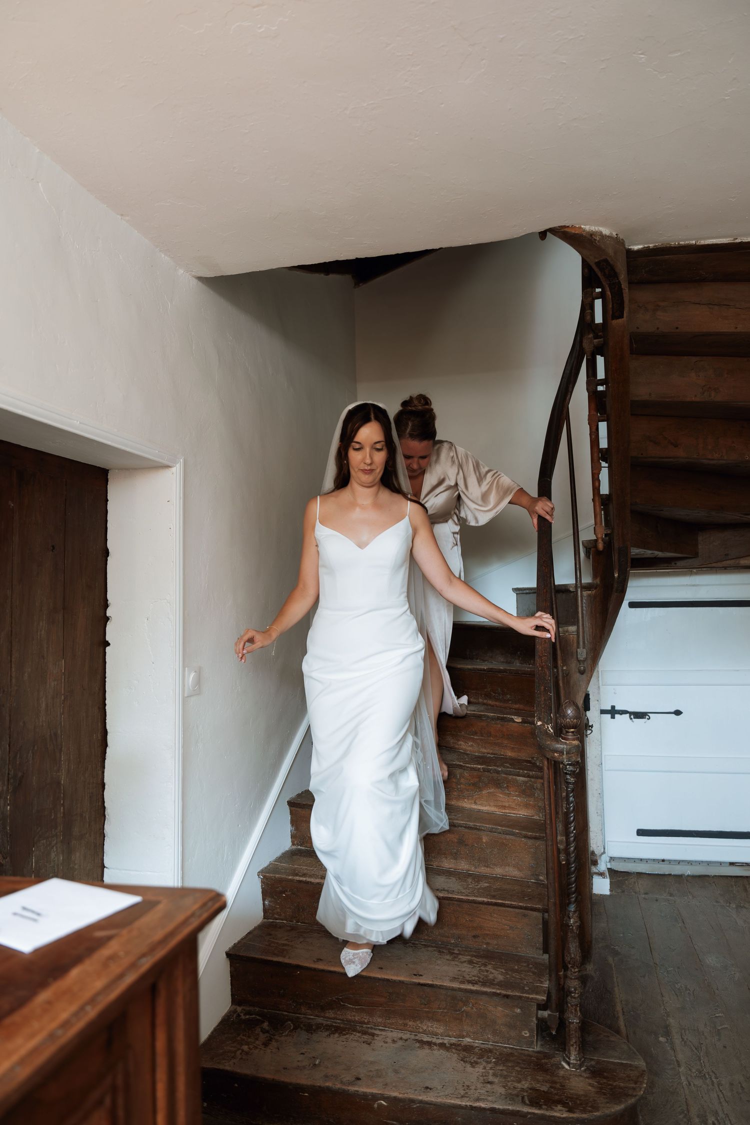 Person in a white dress carefully navigating down rustic wooden stairs.