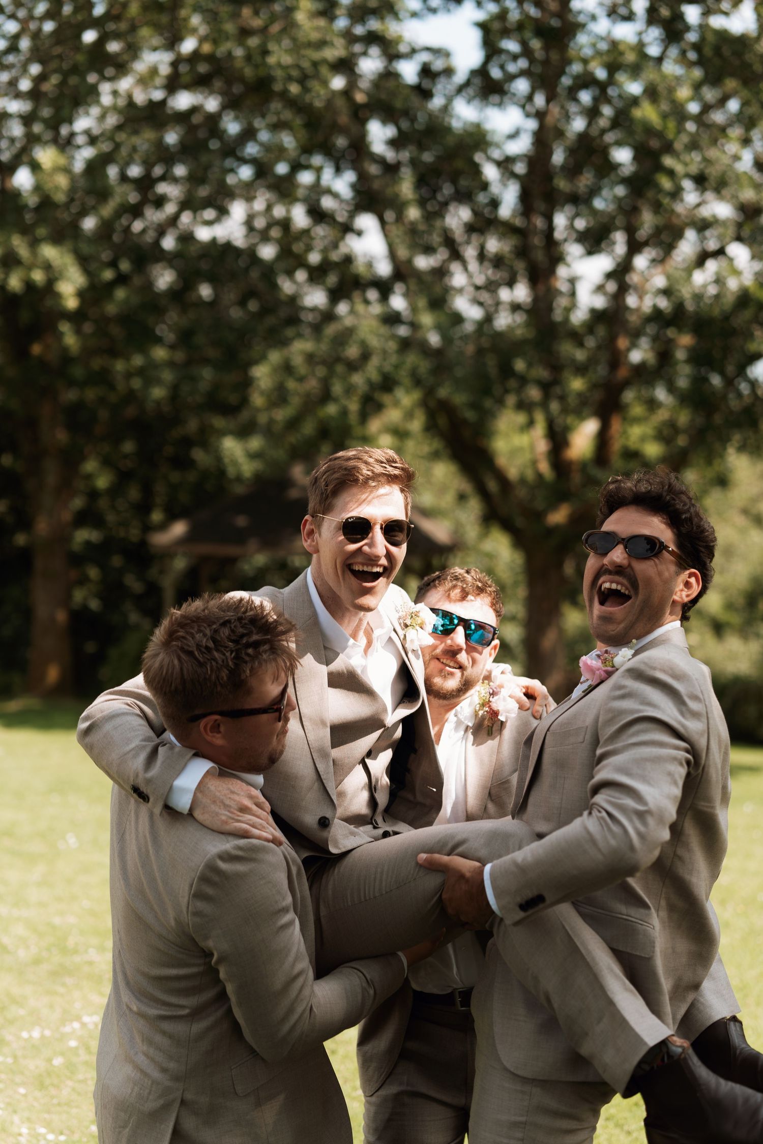 Groomsmen in gray suits laughing and celebrating outdoors.