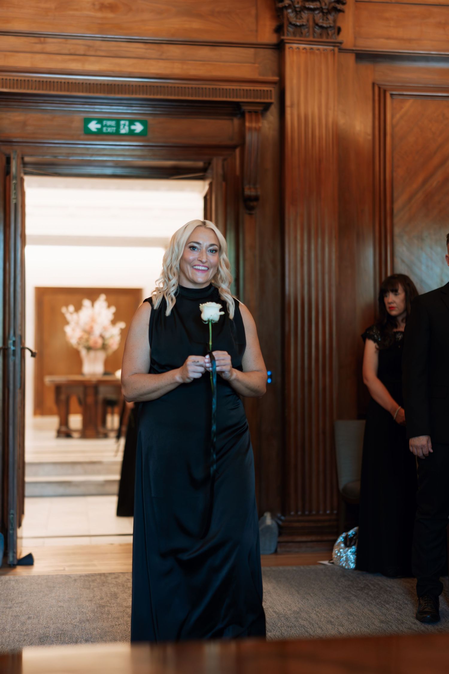 Wedding party members in black dresses walking through an elegant wood-paneled hallway.