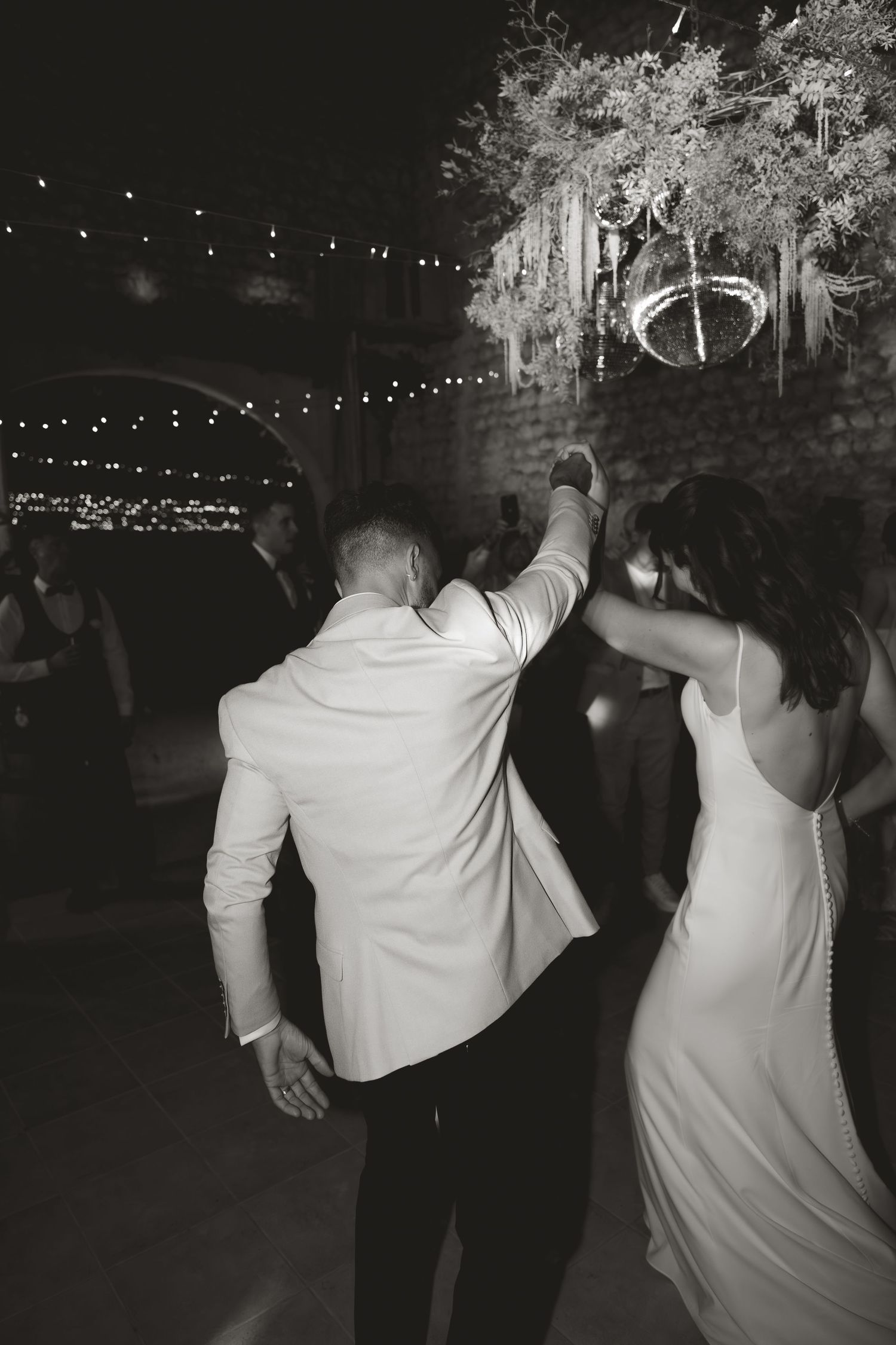 Dancing couple silhouetted against string lights at an evening reception.