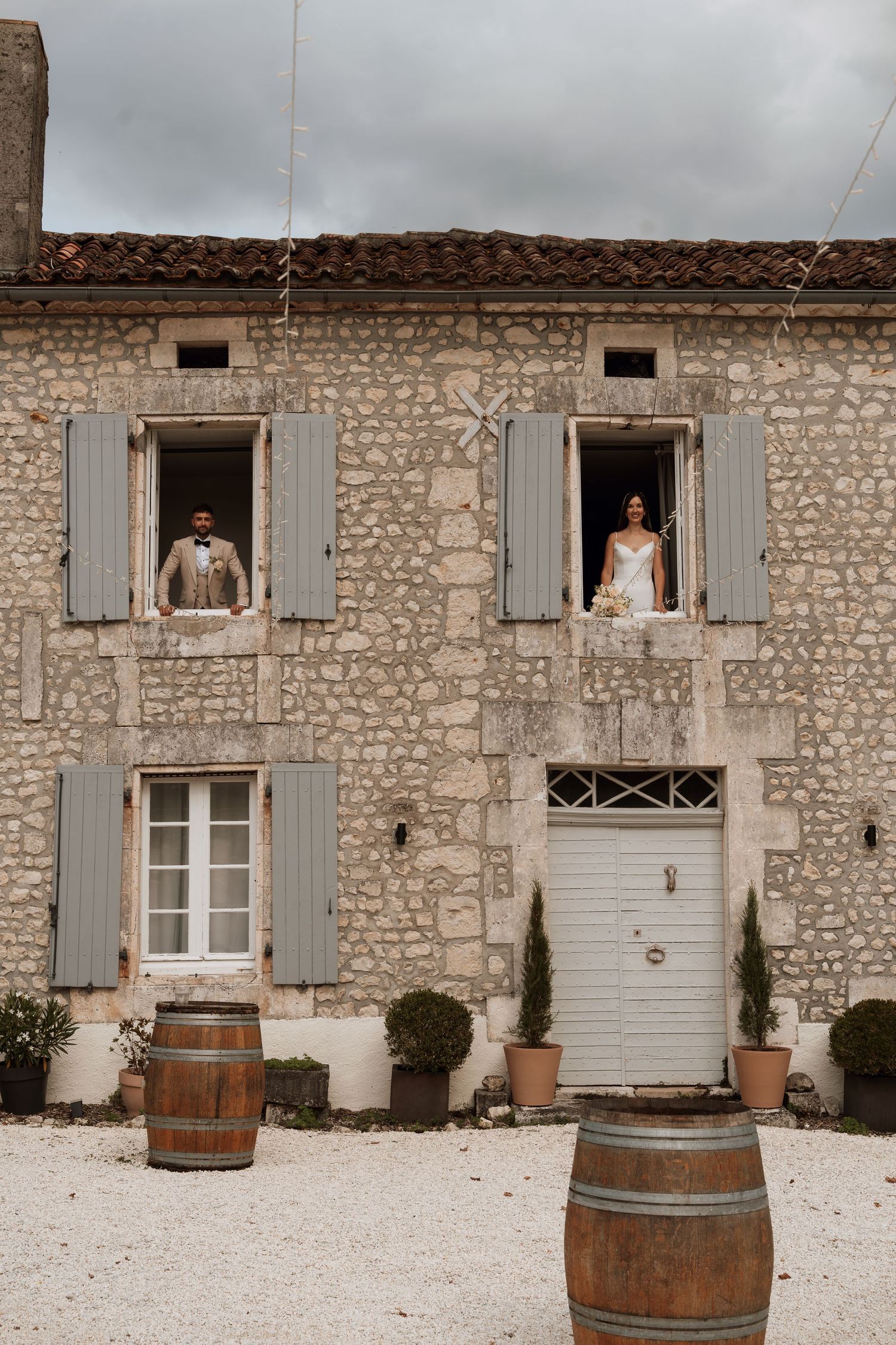 Rustic stone facade of a French country house with wooden shutters and wine barrels.