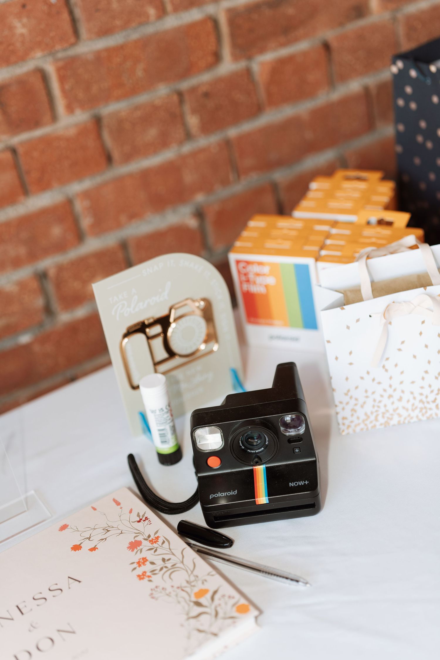 Vintage Polaroid camera and wedding stationery displayed on white table against brick wall.