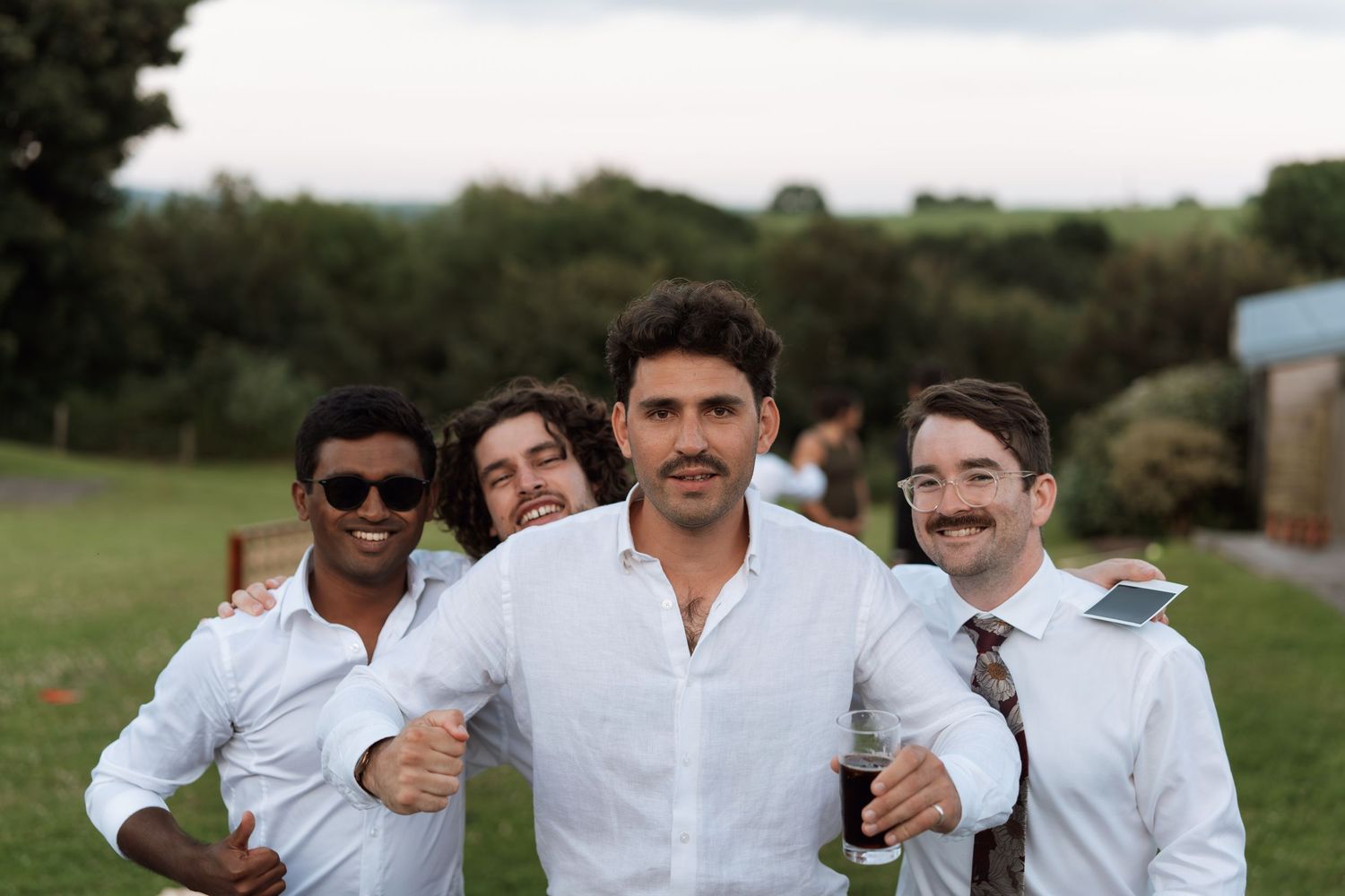 Groomsmen in white shirts posing together outdoors on wedding day.