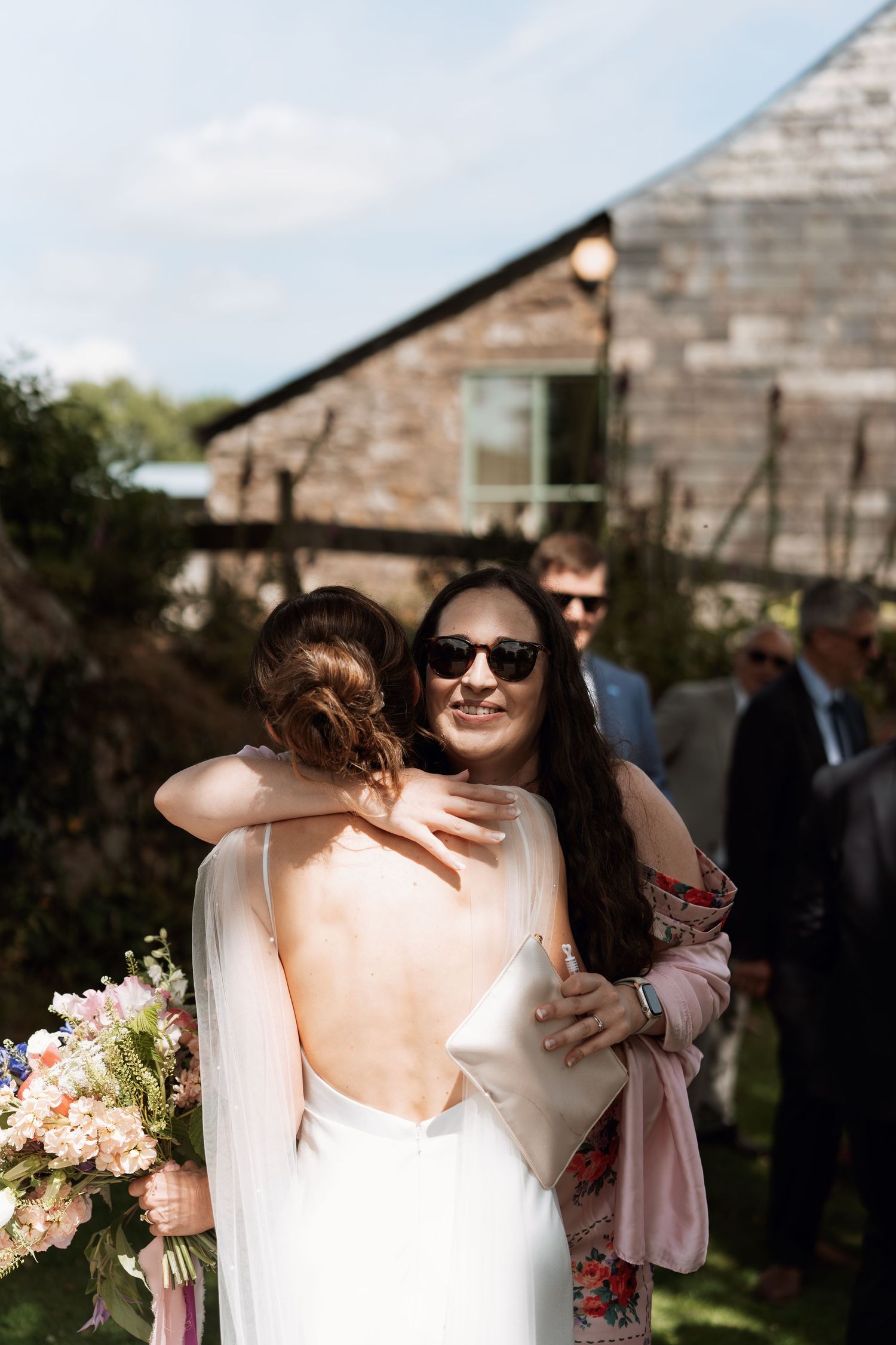 Emotional wedding day embraces shared between guests and the bride outside a stone building.