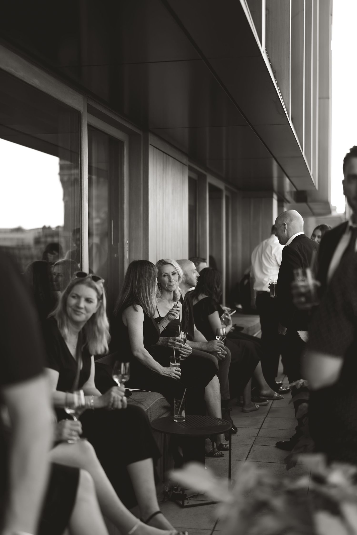 Black and white photo of wedding guests mingling on outdoor terrace.