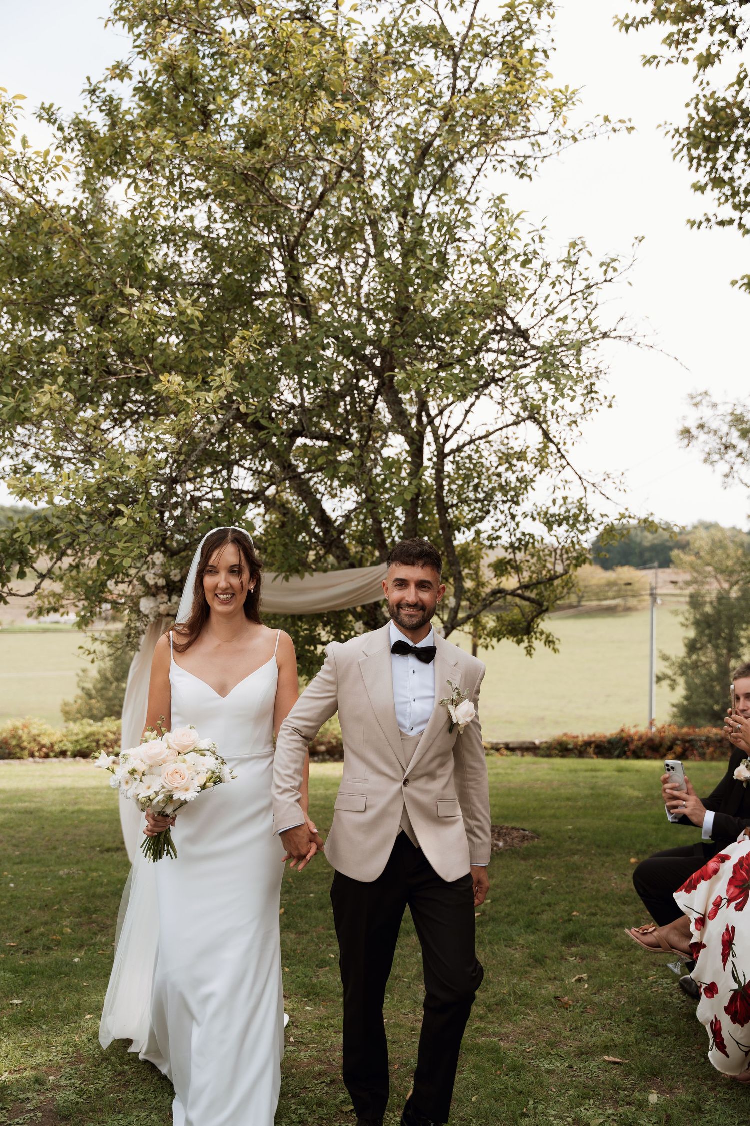 Newlyweds walk hand in hand and celebrate during outdoor garden wedding ceremony.