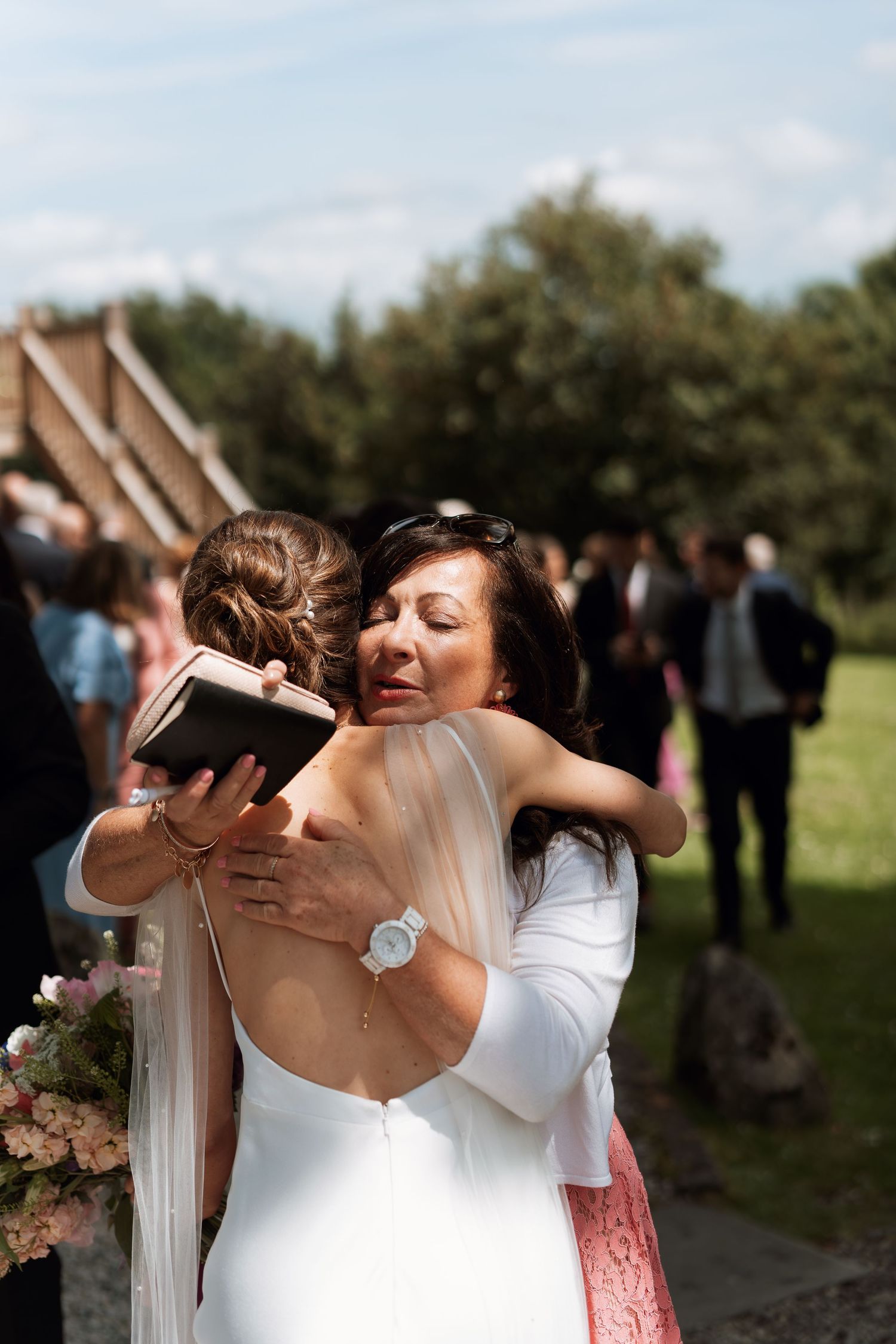 Wedding guests share emotional embraces and hugs during an outdoor celebration.