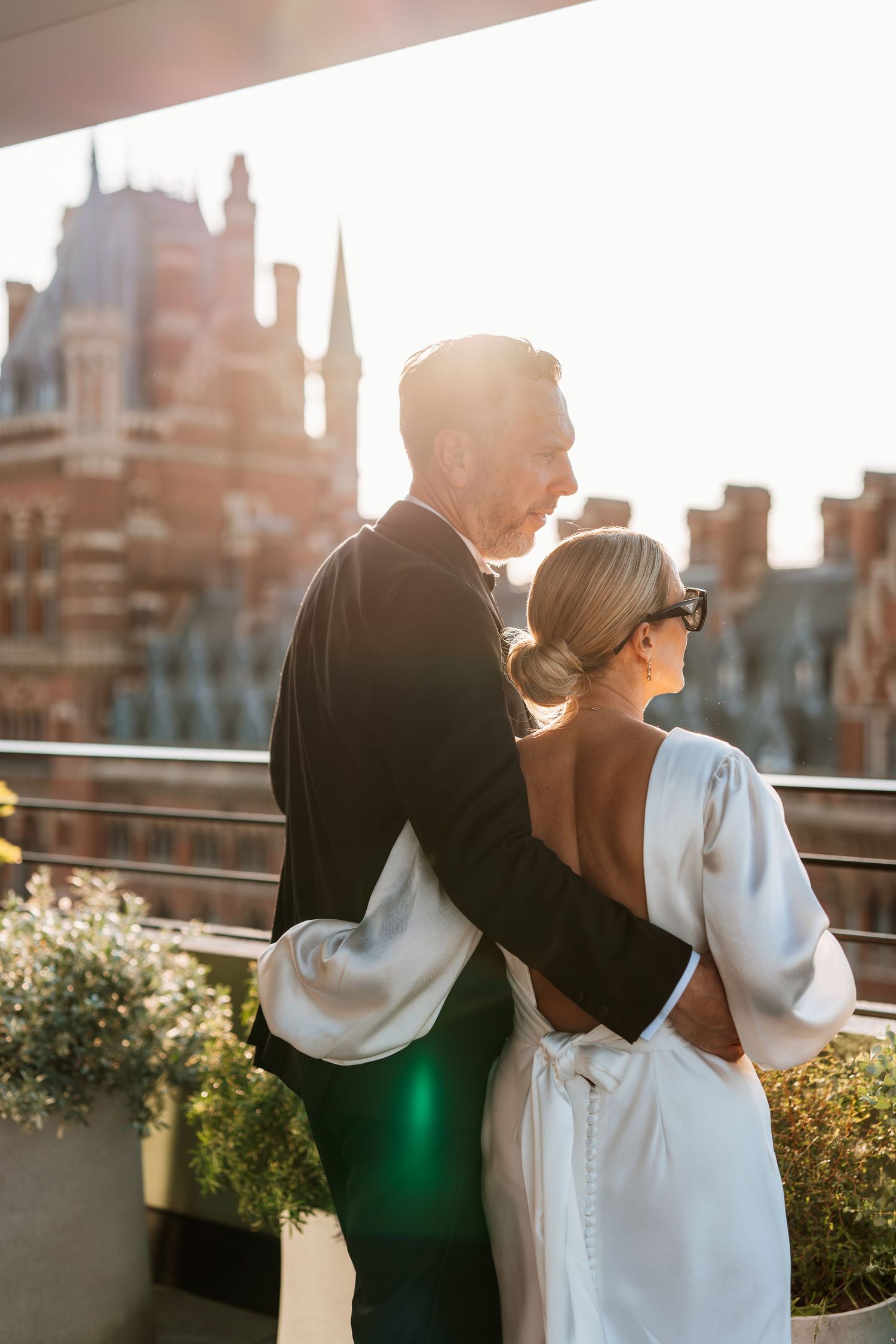 Couple embraces on rooftop terrace with city skyline at sunset.
