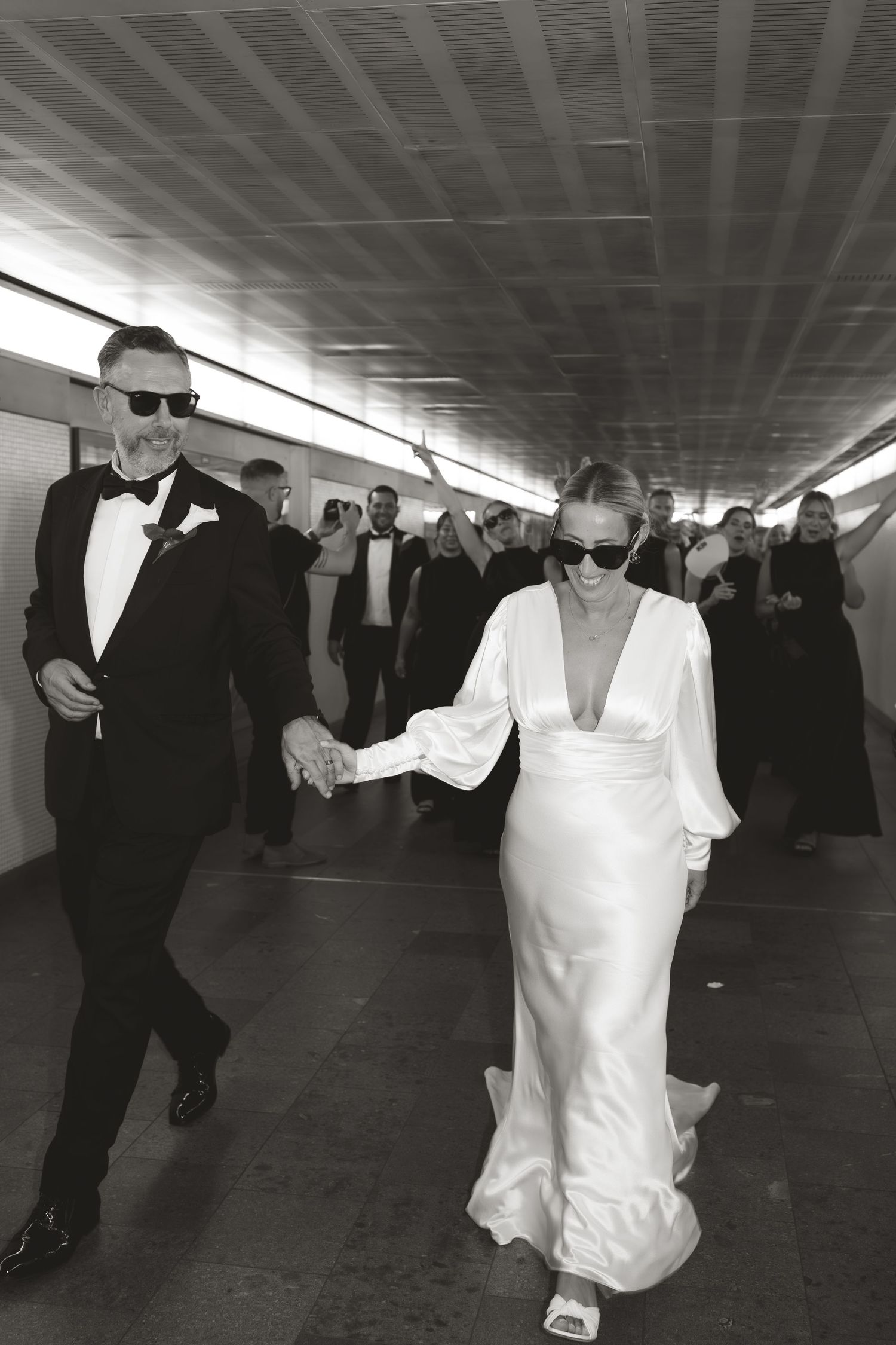 Wedding guests in formal attire dance in a long hallway.