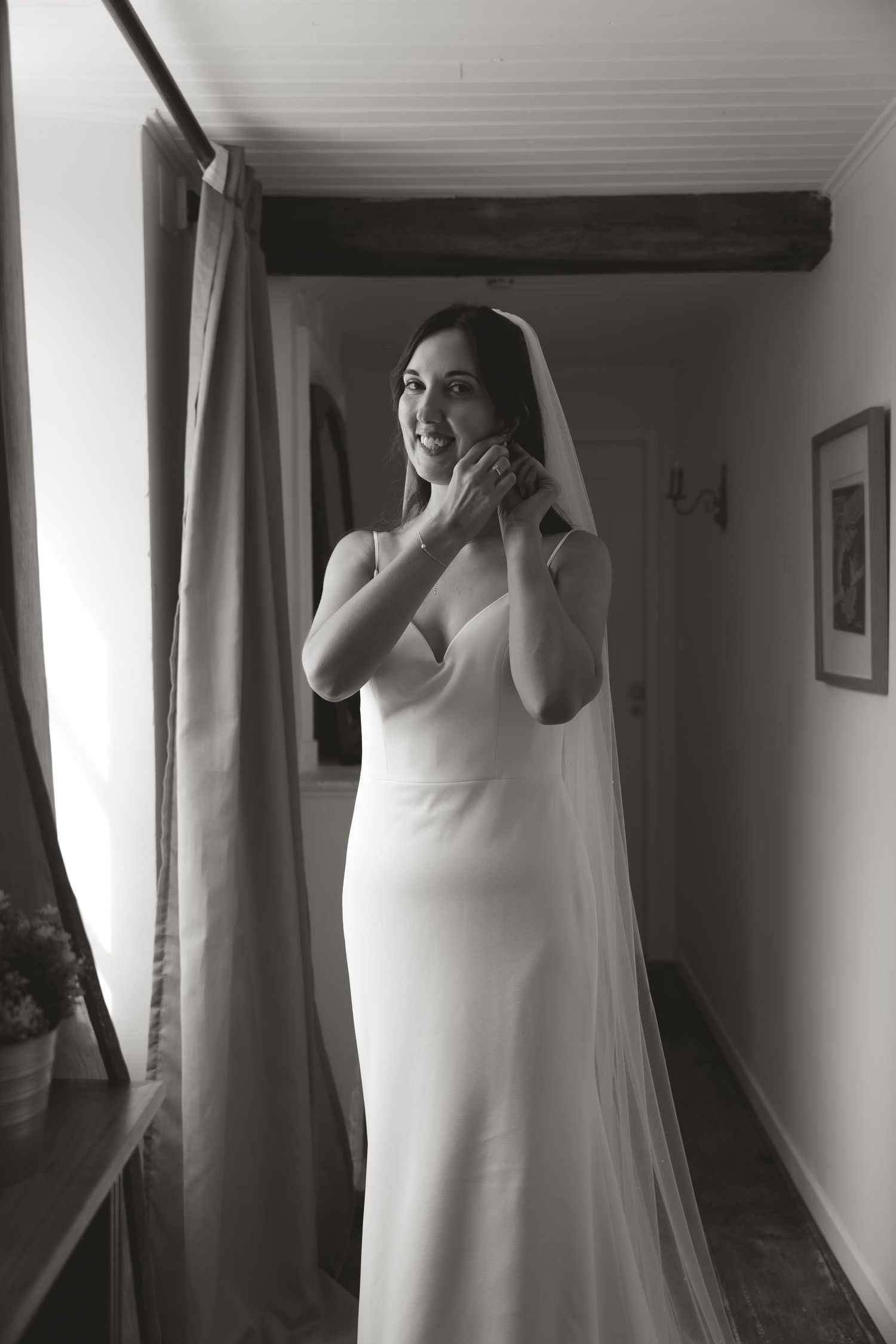 Bride in white dress and veil standing in hallway with dramatic lighting.